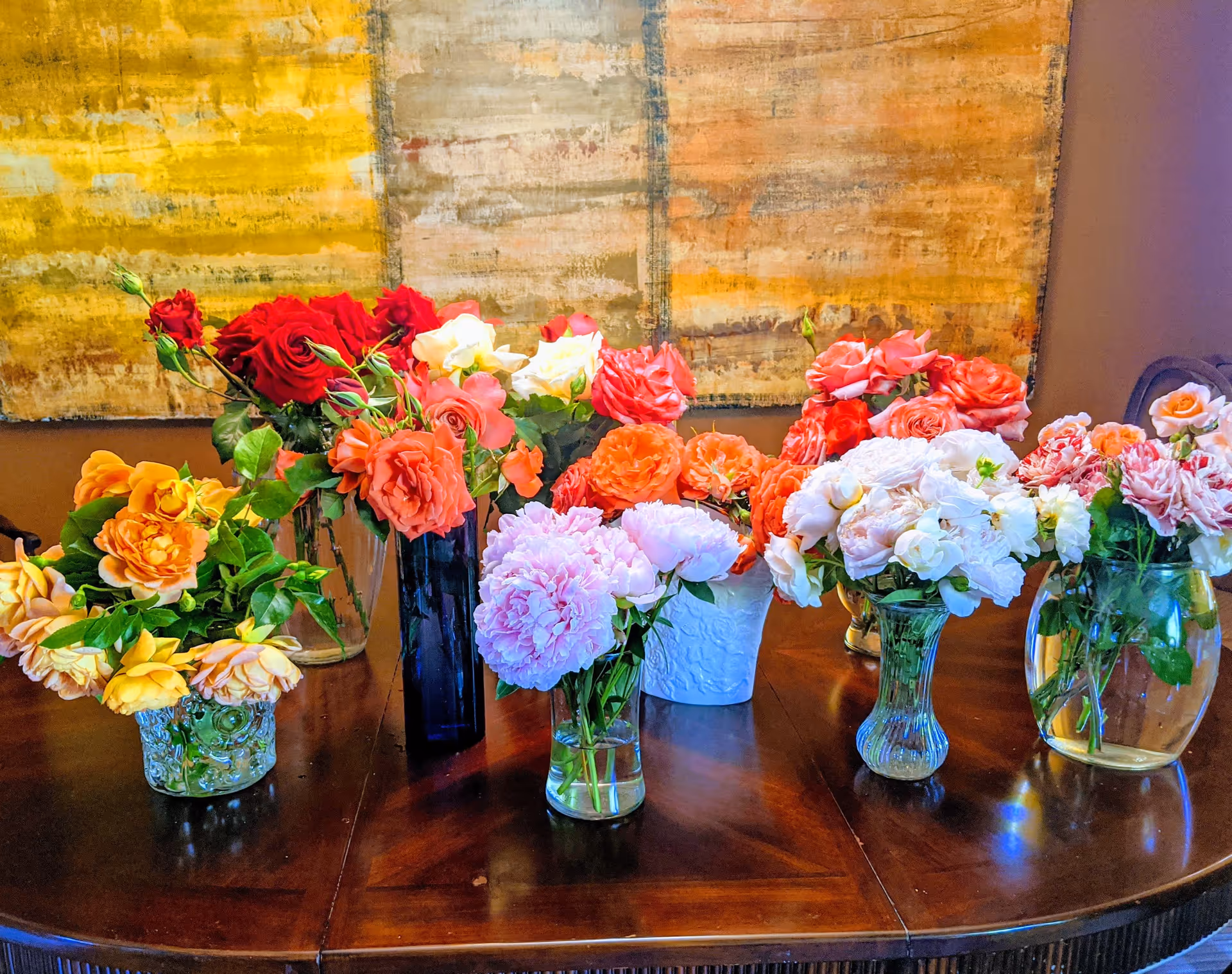 Vibrant mixed flowers in glass vases arranged on a dark wooden table indoors.