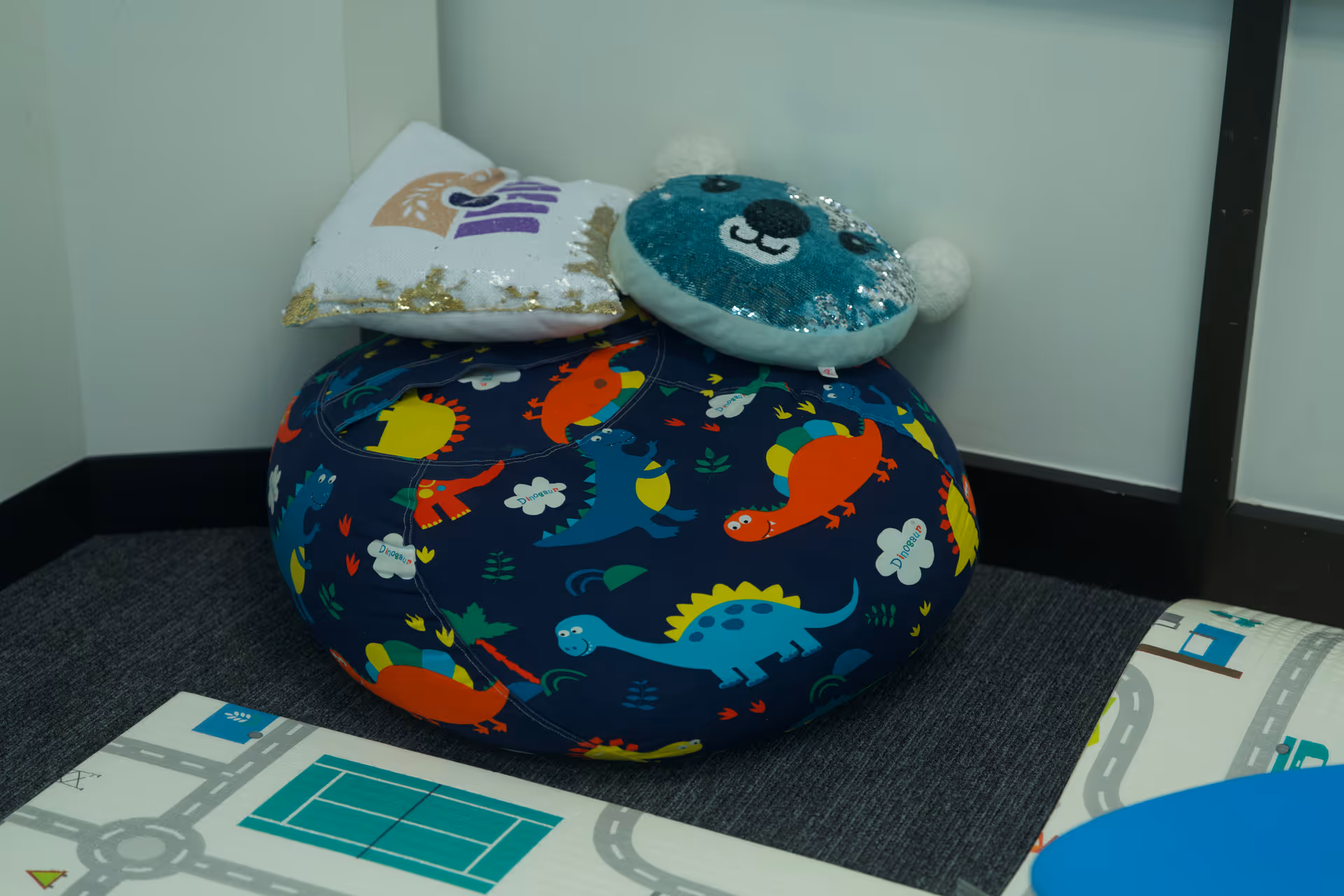 Colorful round bean bag with dinosaur print and sparkly pillows in a children's play area.