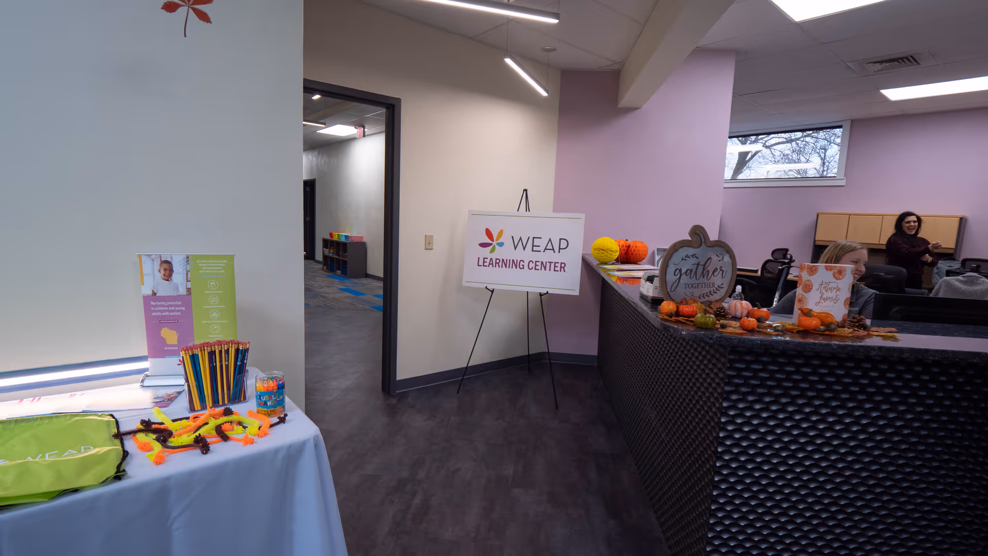 Interior lobby with WEAP Learning Center sign, reception counter, autumn decorations, and attendees in background.