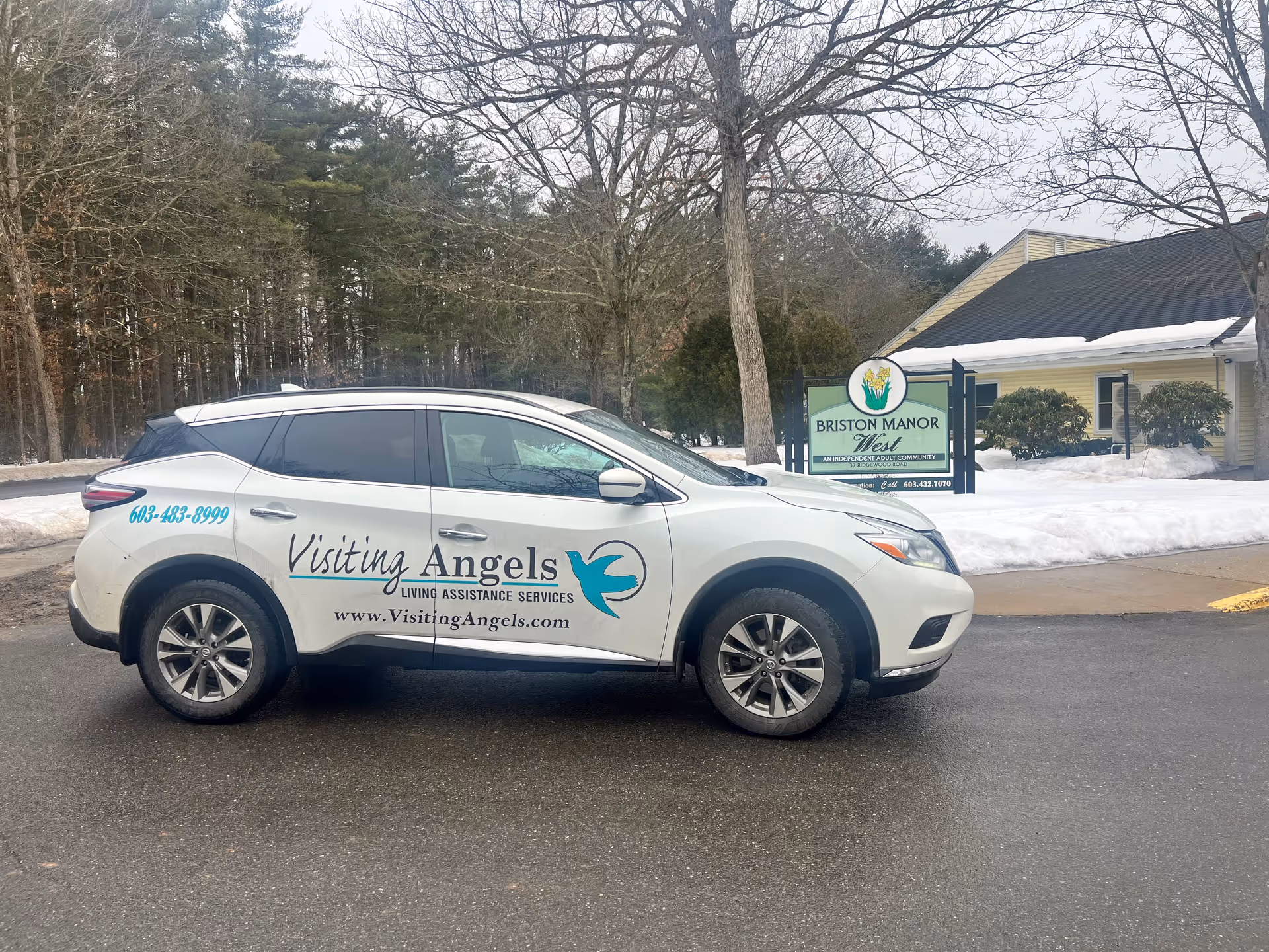 White Visiting Angels car parked outside a beige building in a snowy setting