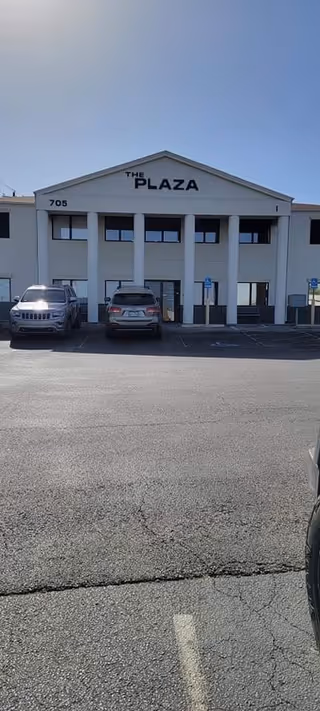 Front view of a building named The Plaza with parked cars.