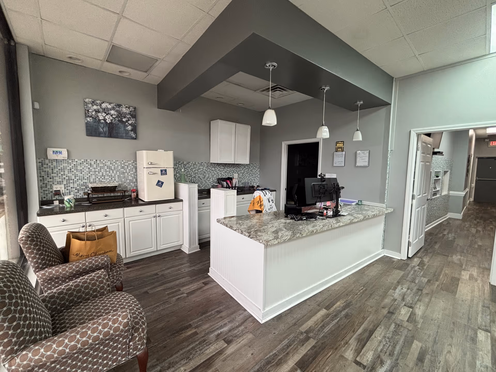 Reception desk with marble countertop, white cabinets, pendant lights, and waiting chairs in an interior corridor.