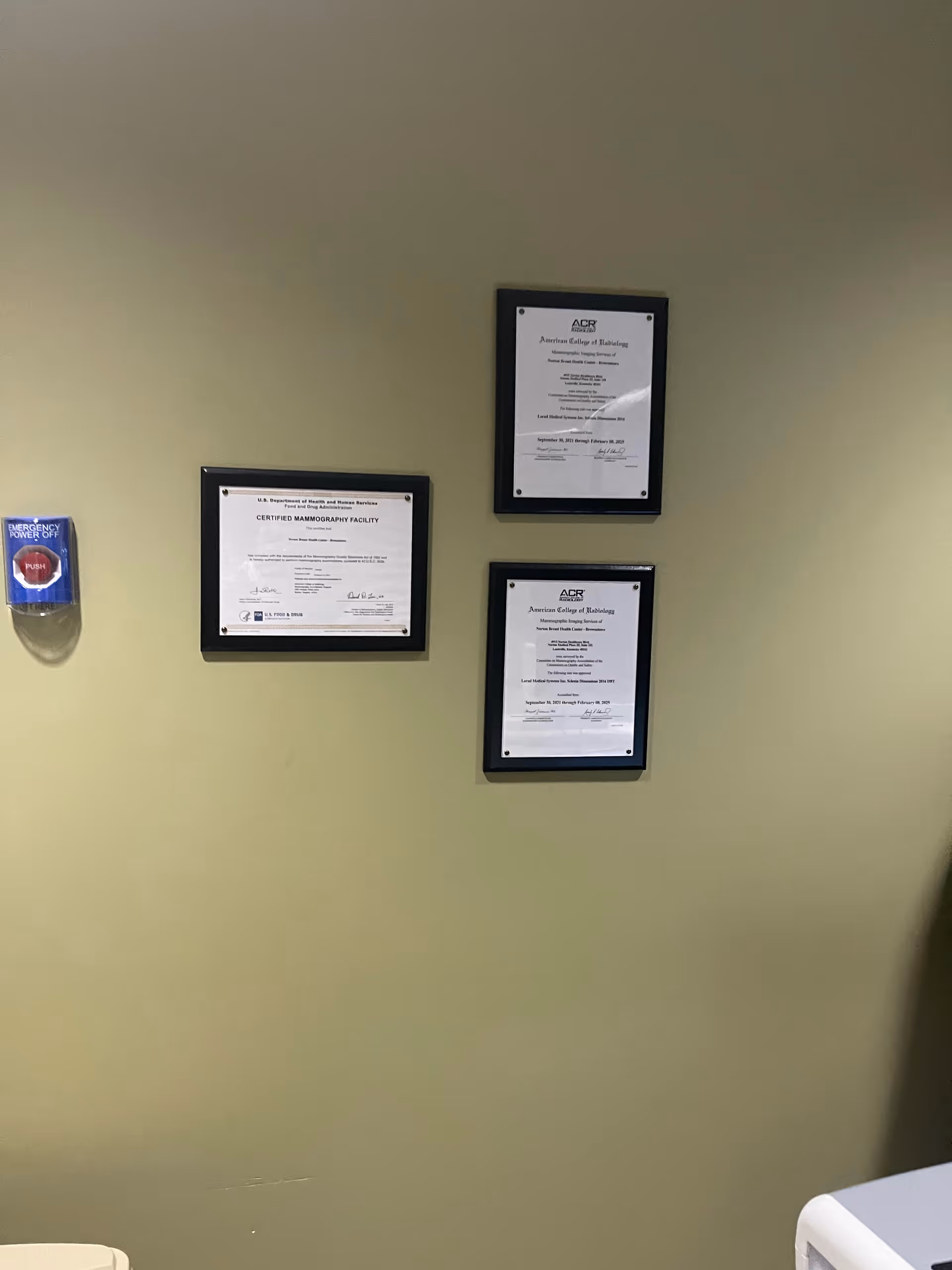 Interior wall displays framed certificates and a red emergency power-off switch.