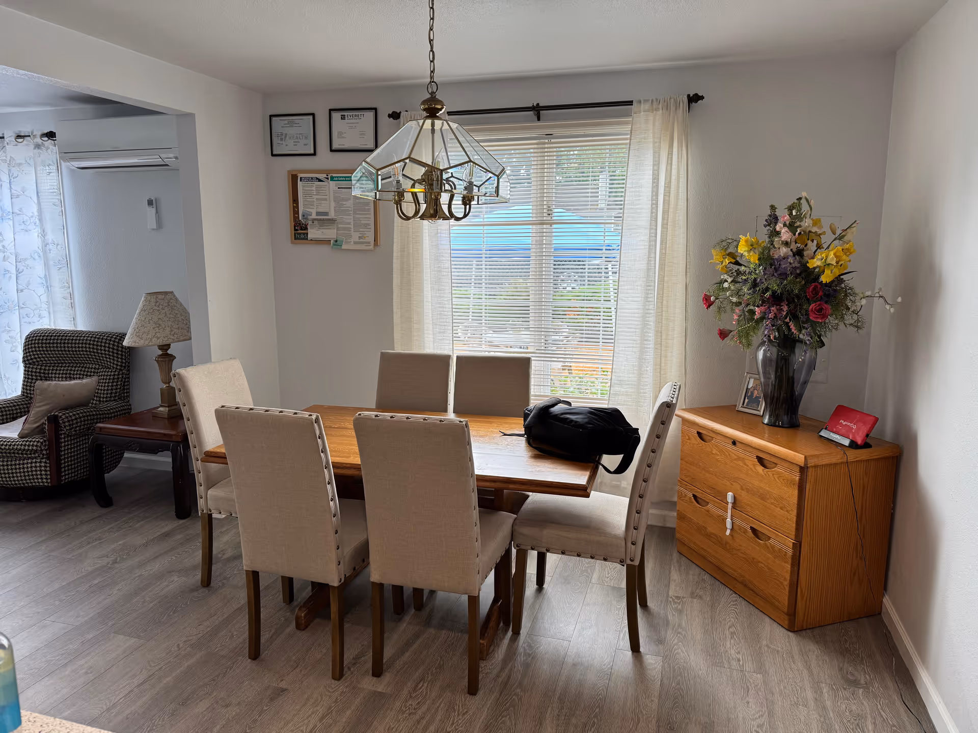 A dining room with a wooden table, beige chairs, chandelier, and a floral vase.