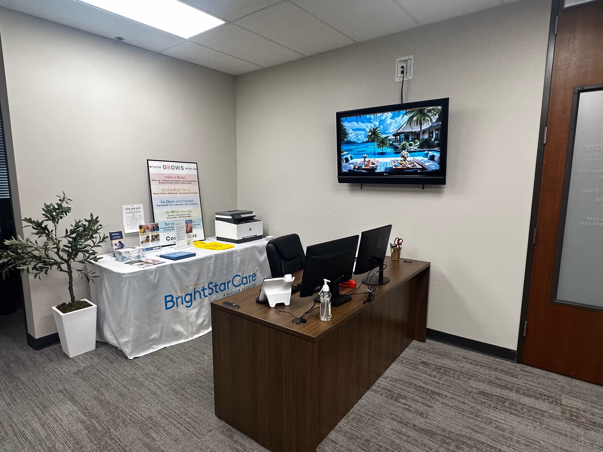 Reception area with BrightStarCare branded table, desk, monitors, plant, and wall-mounted TV