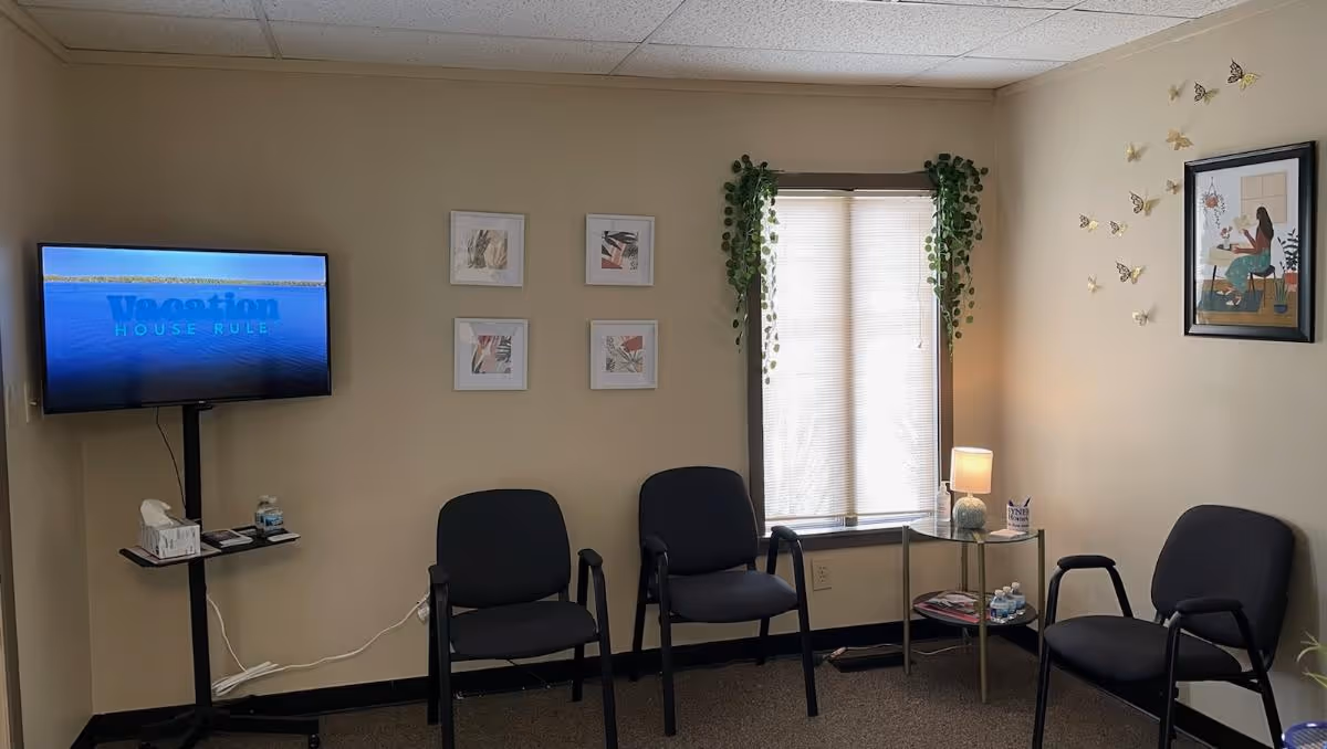 A small senior living common area with chairs, a wall-mounted TV, and a window.