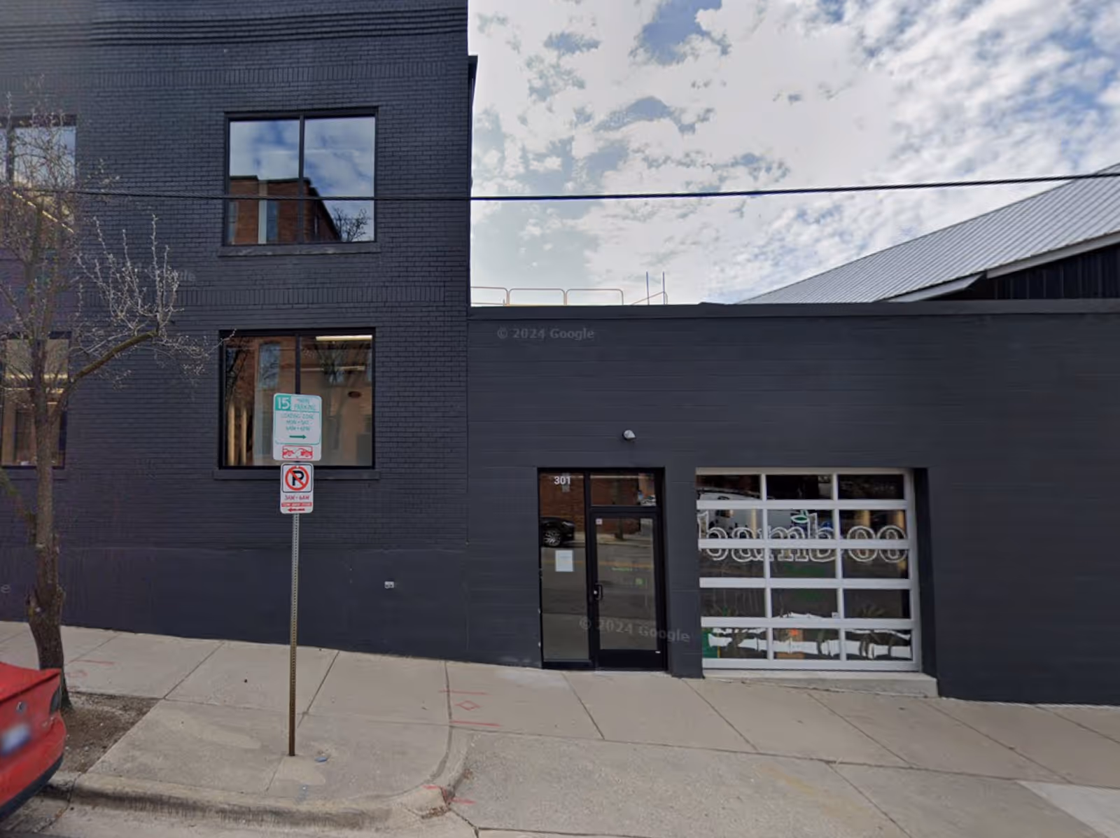 Dark brick building with glass door and large storefront windows along a sidewalk.