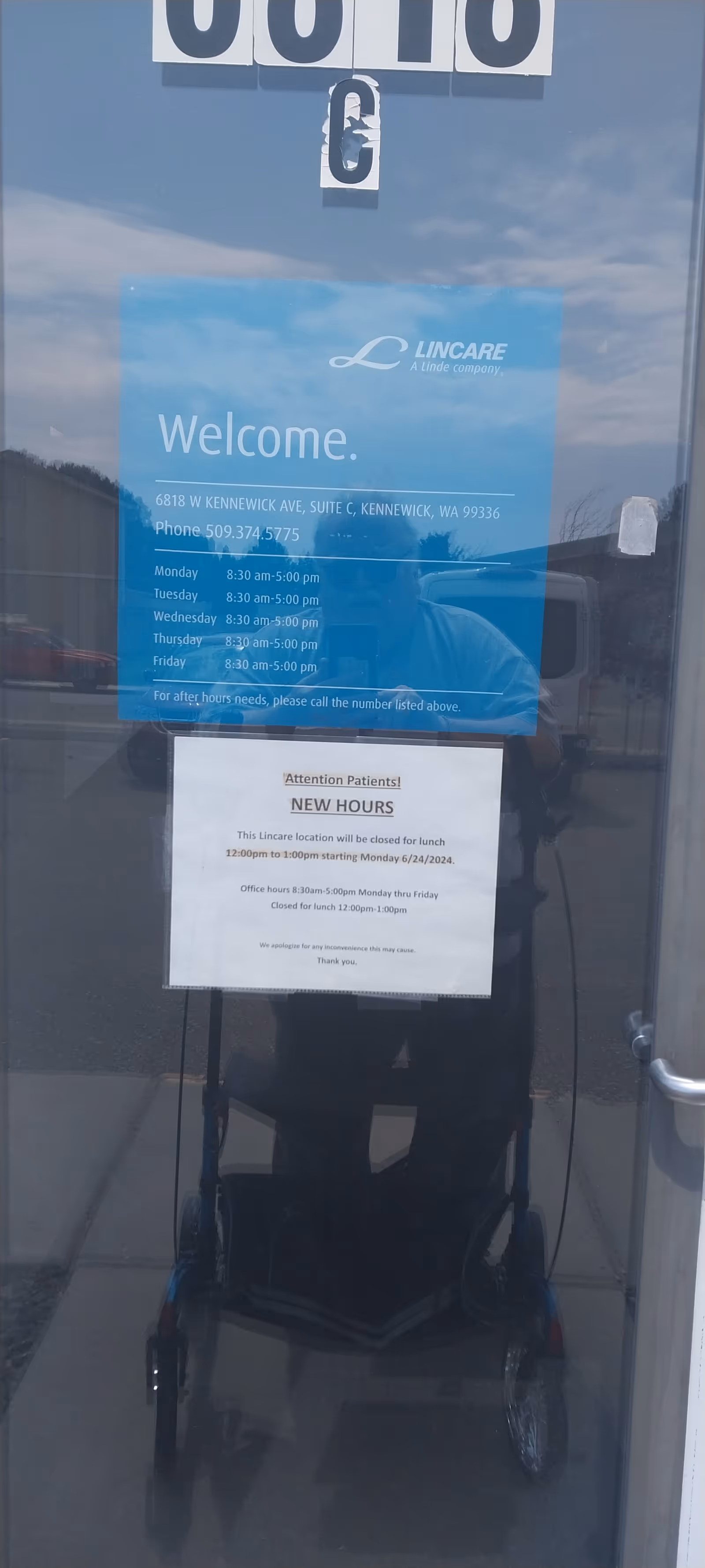 Glass door with LINCARE welcome sign and posted hours; a wheelchair is reflected inside.