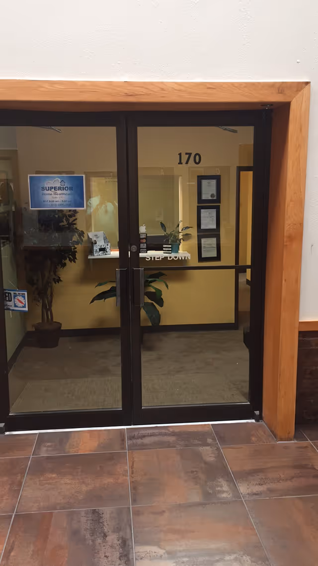 Glass double doors open into a lobby showing plants, a reception desk, and wall certificates.