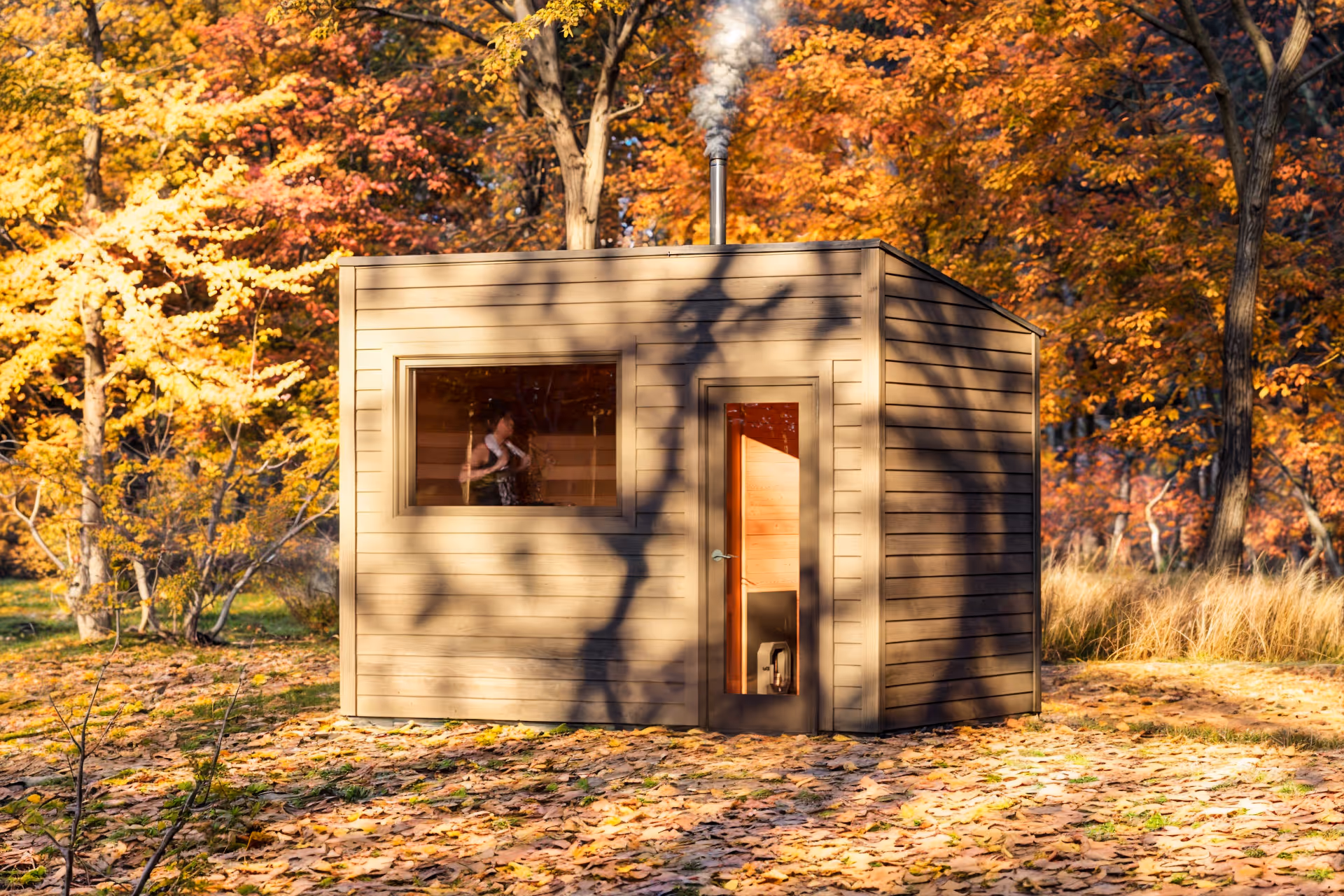 A small wooden sauna hut sits in a forest with autumn leaves on the ground.