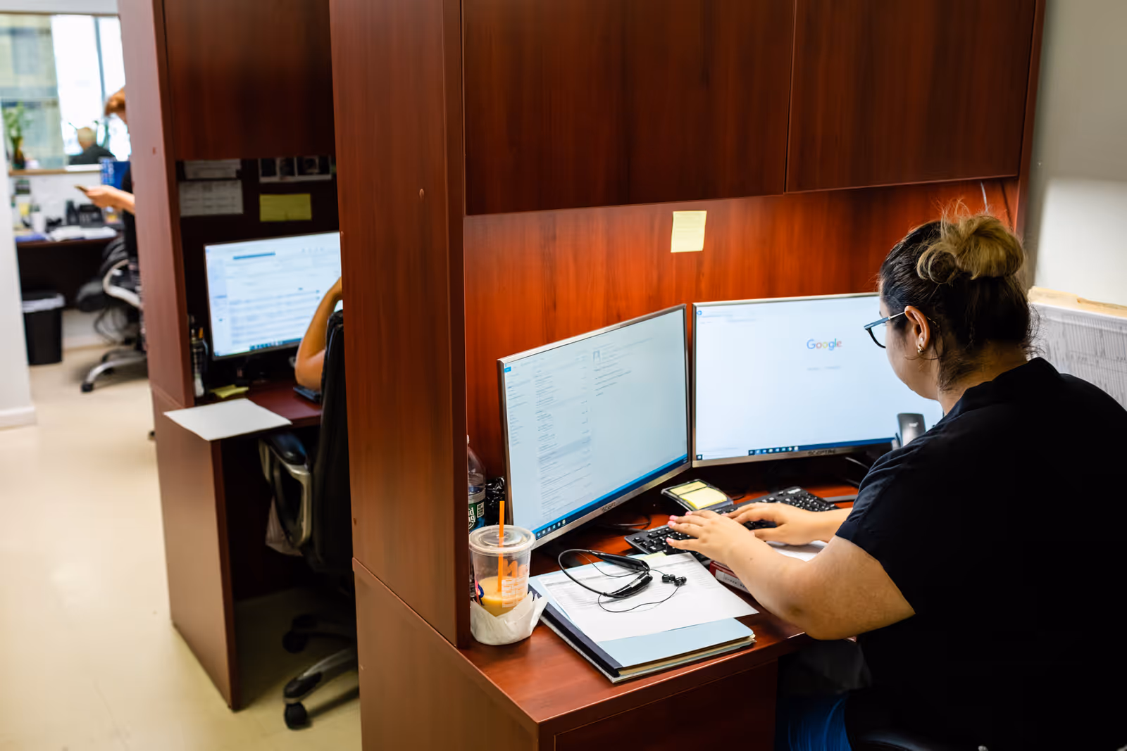 Caregiver at a desk with dual monitors in a wooden office cubicle at a care facility