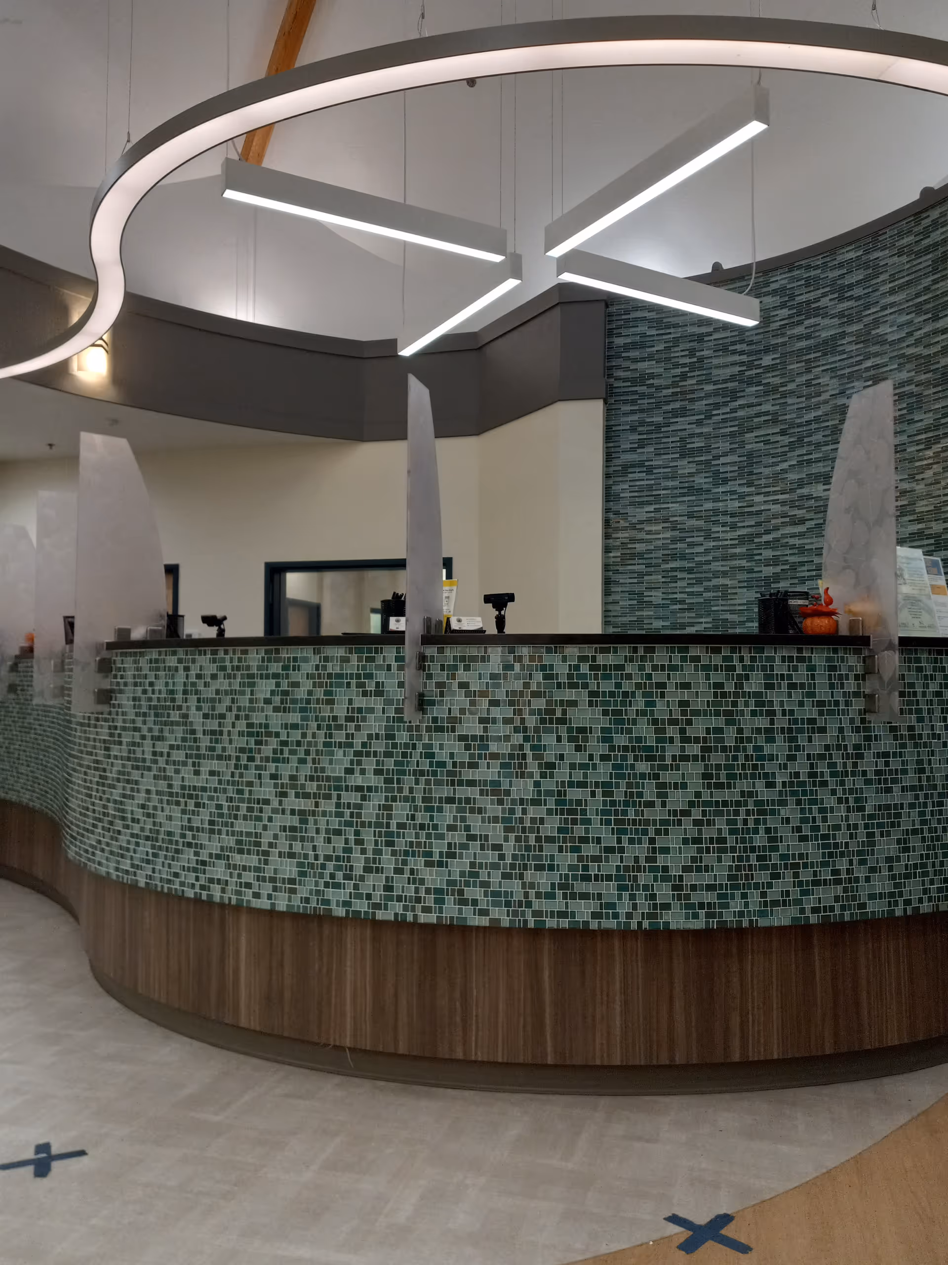 Modern curved reception desk with green mosaic tiles in a facility lobby.