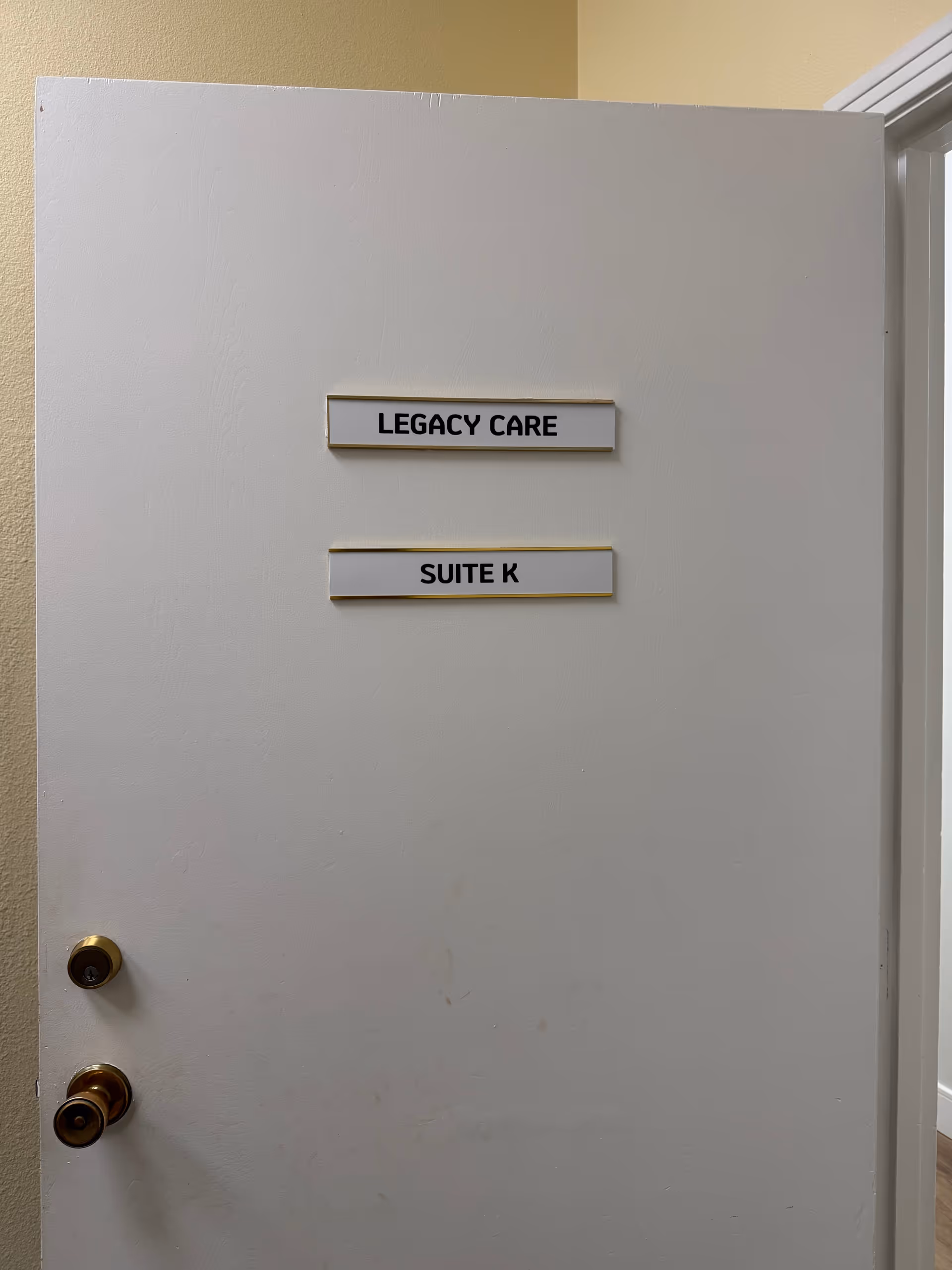 White interior door with Legacy Care and Suite K signs in a hallway.