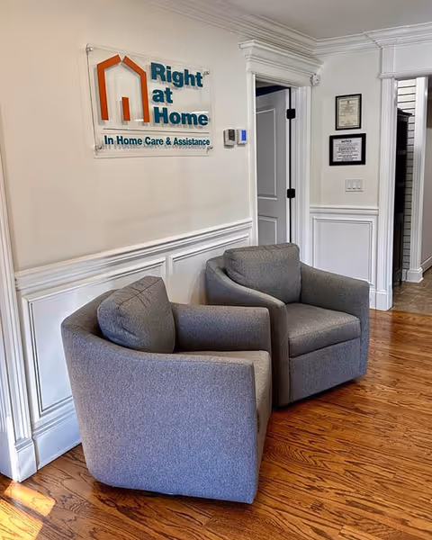 Two gray armchairs sit in a white-walled lobby with a Right at Home sign.