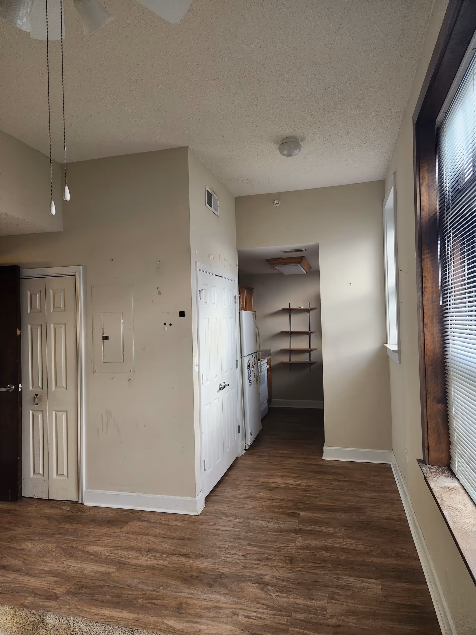 Narrow interior kitchen area with fridge, cabinets, and open shelving along beige walls.