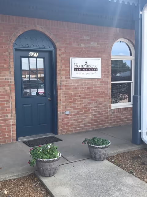 Brick building exterior with a blue door, arched window, and Home Instead sign.