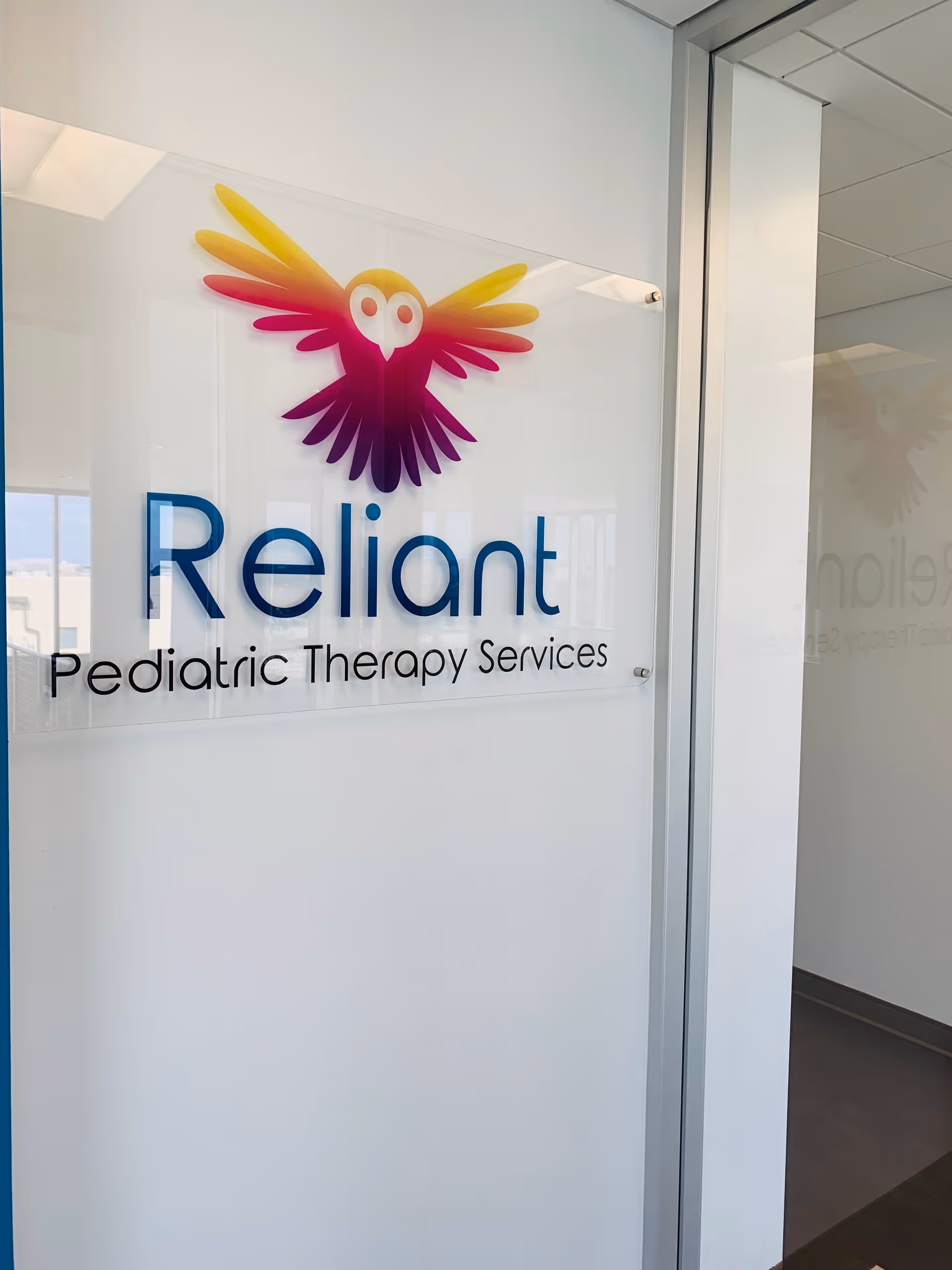 Clear glass sign reads 'Reliant Pediatric Therapy Services' with a colorful owl logo.