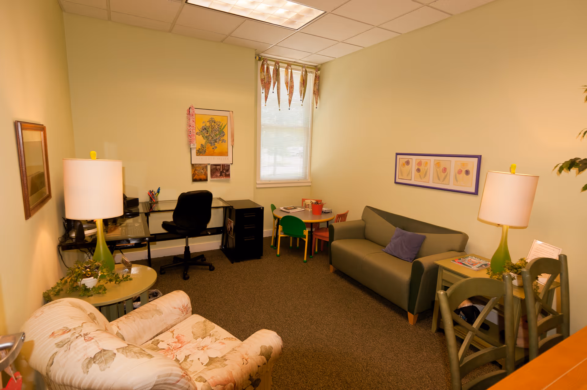 Cozy senior living common area with sofa, desk, tables, lamps, and wall art.
