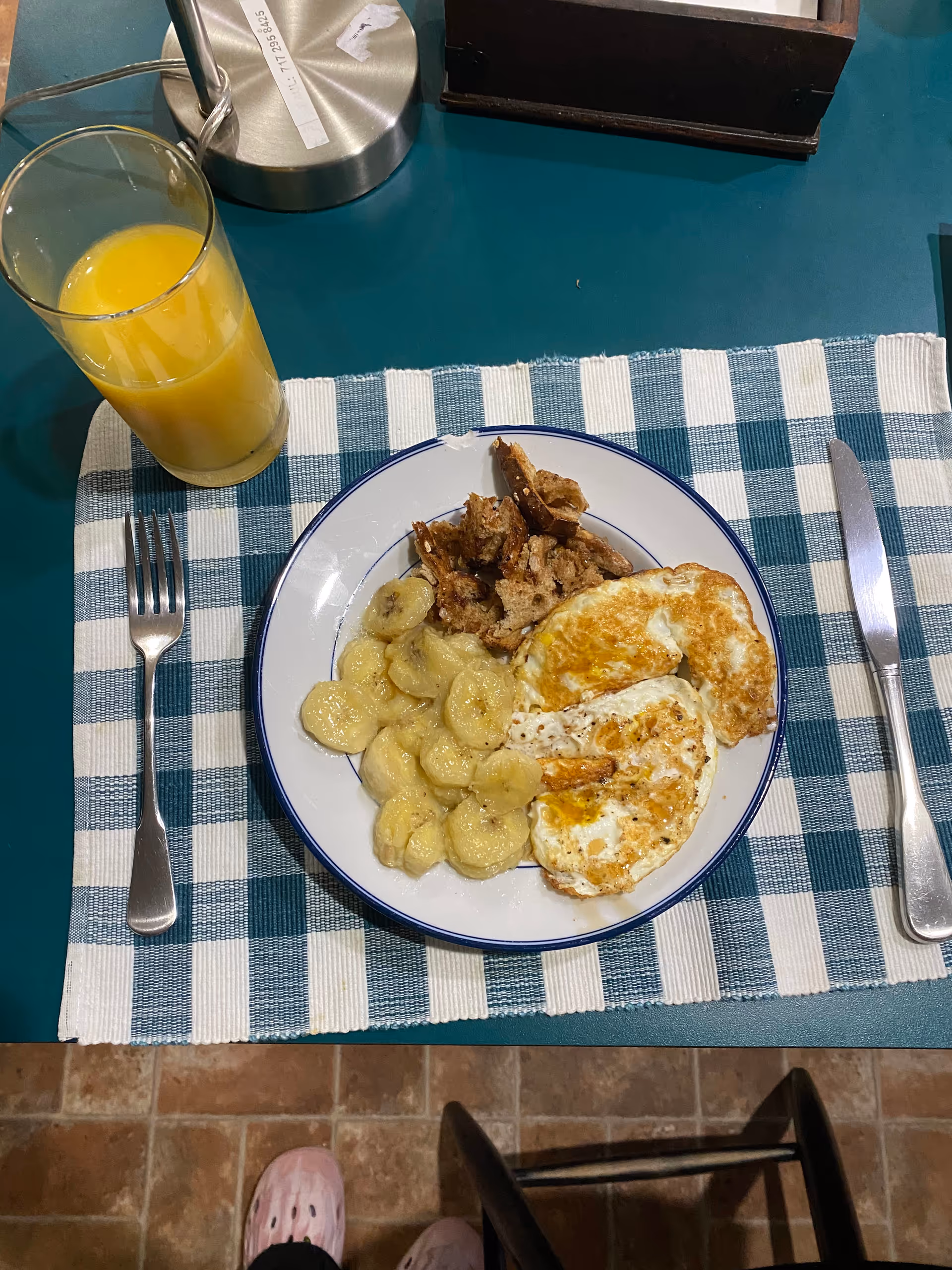 Plate with fried eggs, potatoes, meat, and orange juice on a teal dining table.