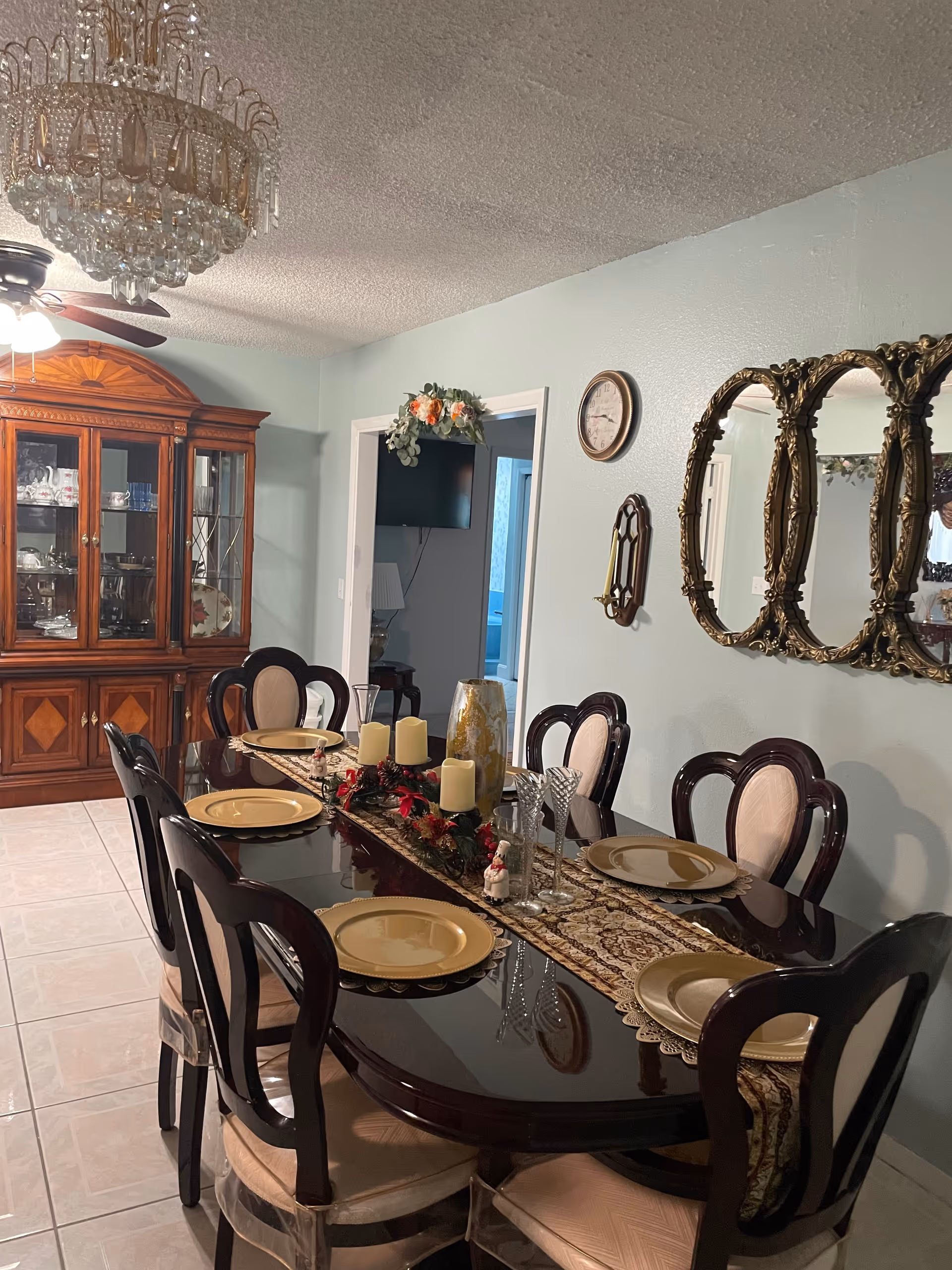 Elegant dining room with a long table set for a meal, chandelier, and china cabinet.