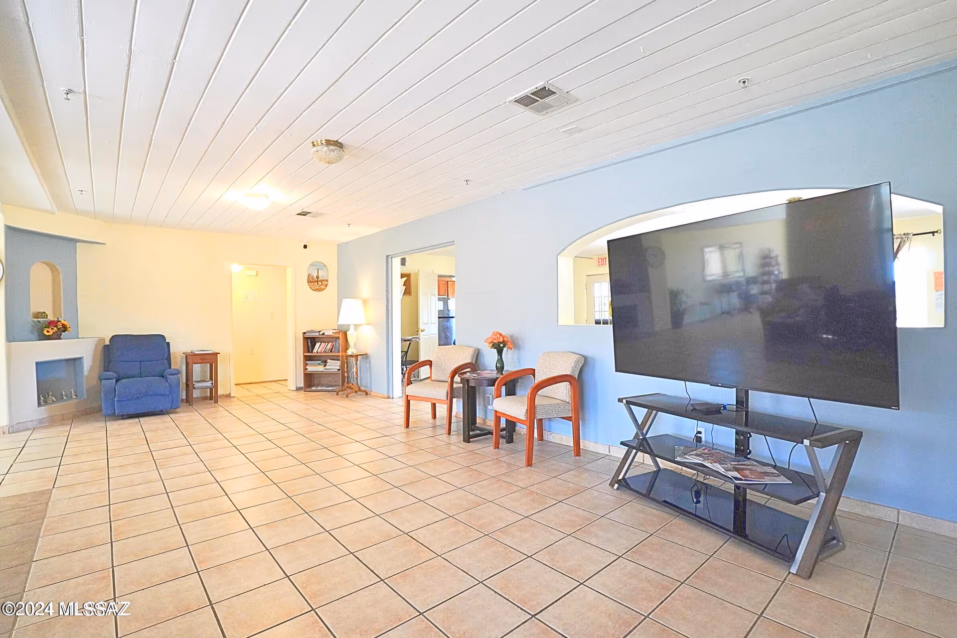 Spacious senior living common area with blue walls, tiled floor, seating, and a large TV.