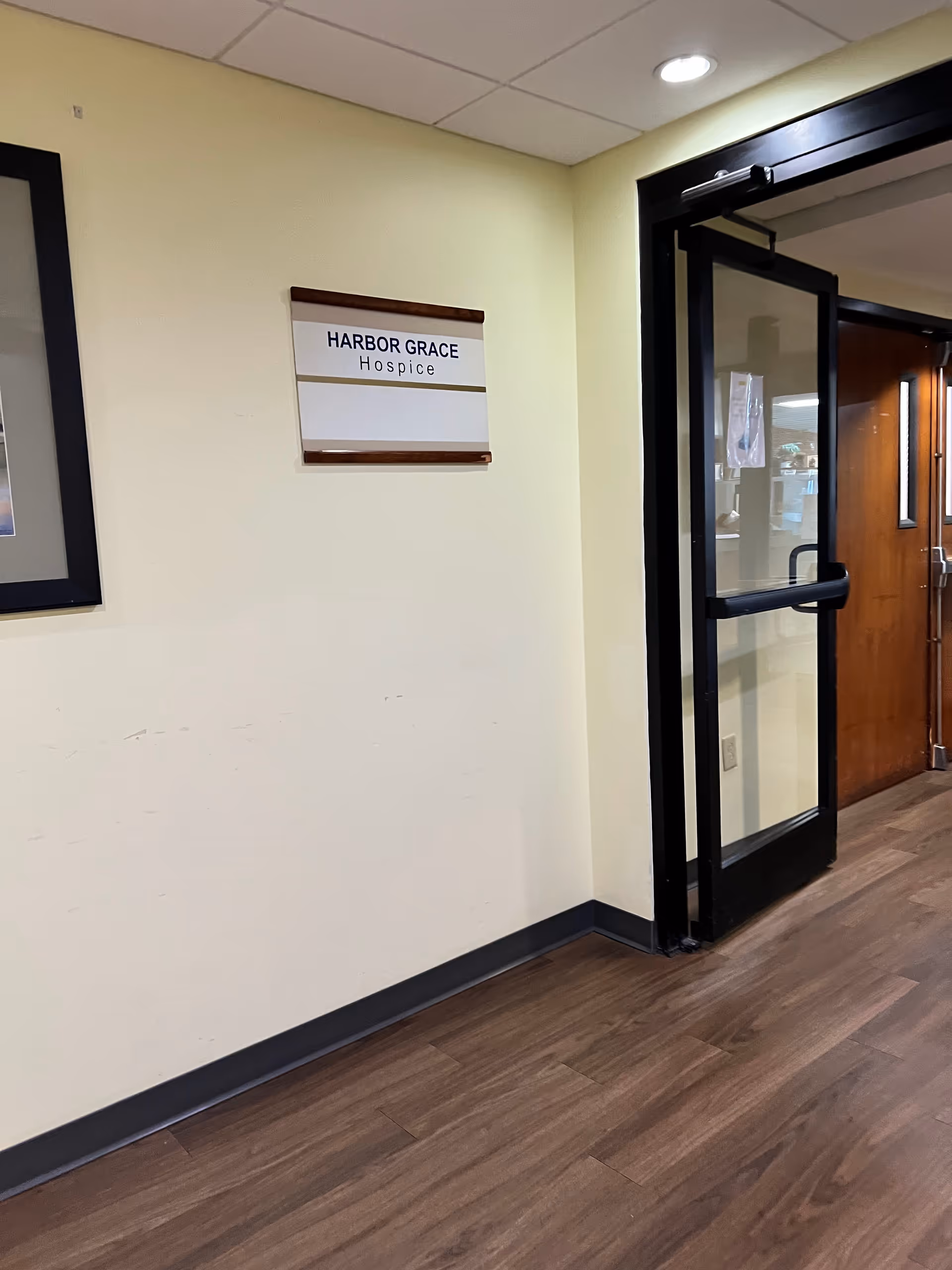 A hallway inside Harbor Grace Hospice with a glass door and wall sign.