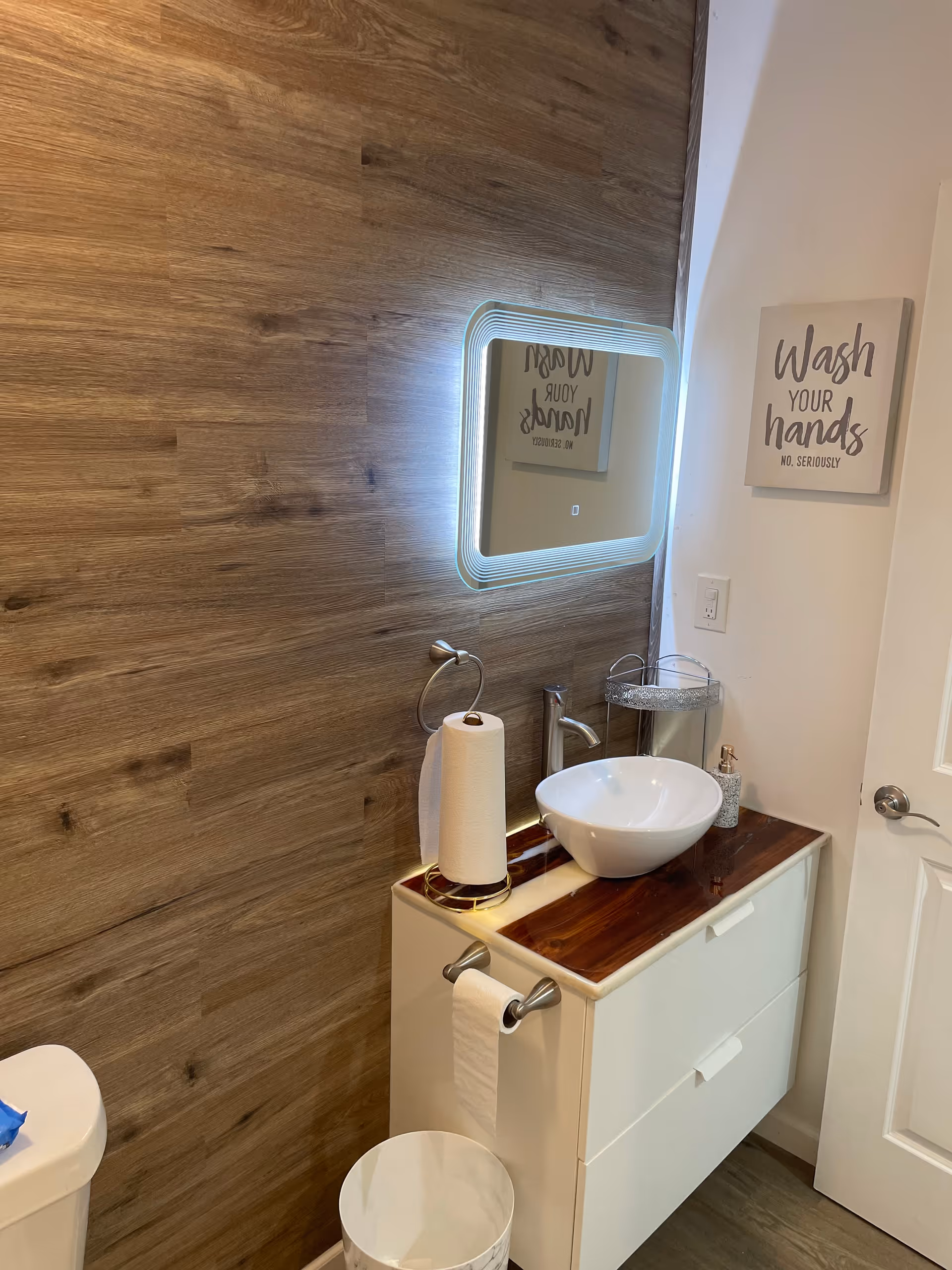 Modern bathroom vanity with vessel sink, illuminated mirror, and wash-your-hands sign.