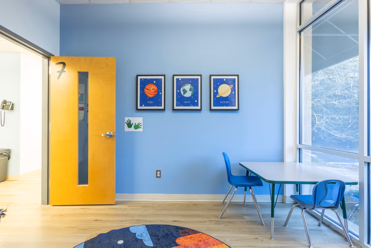 Blue-walled classroom with door labeled seven, space-themed art, table and chairs by window.
