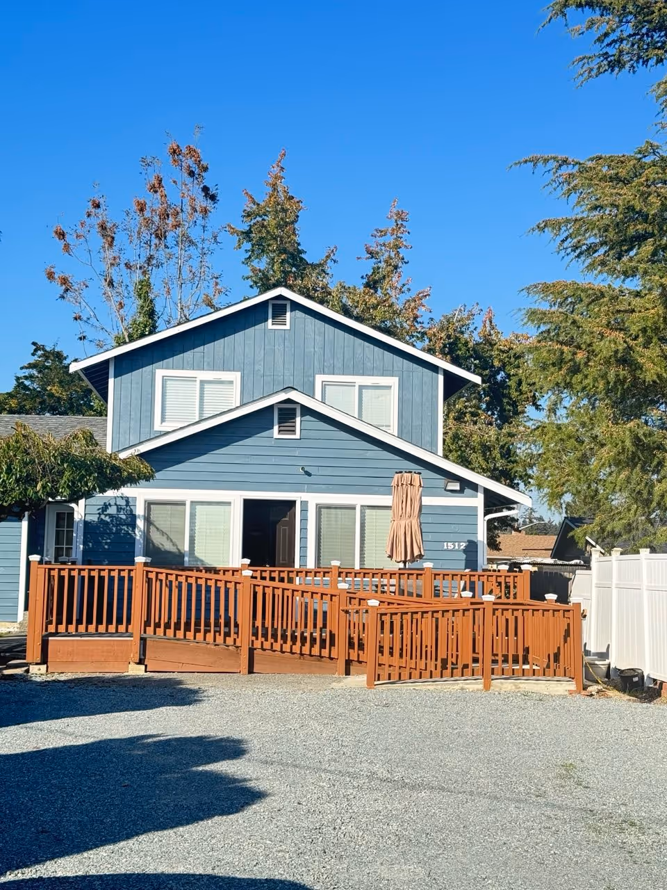Blue two-story facility with wooden deck railing, umbrella, and white fence outdoors.