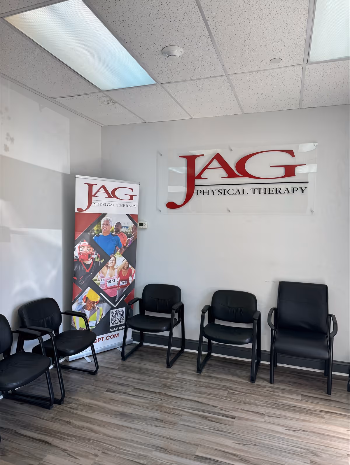 Waiting area with black chairs and a JAG Physical Therapy banner on the wall.