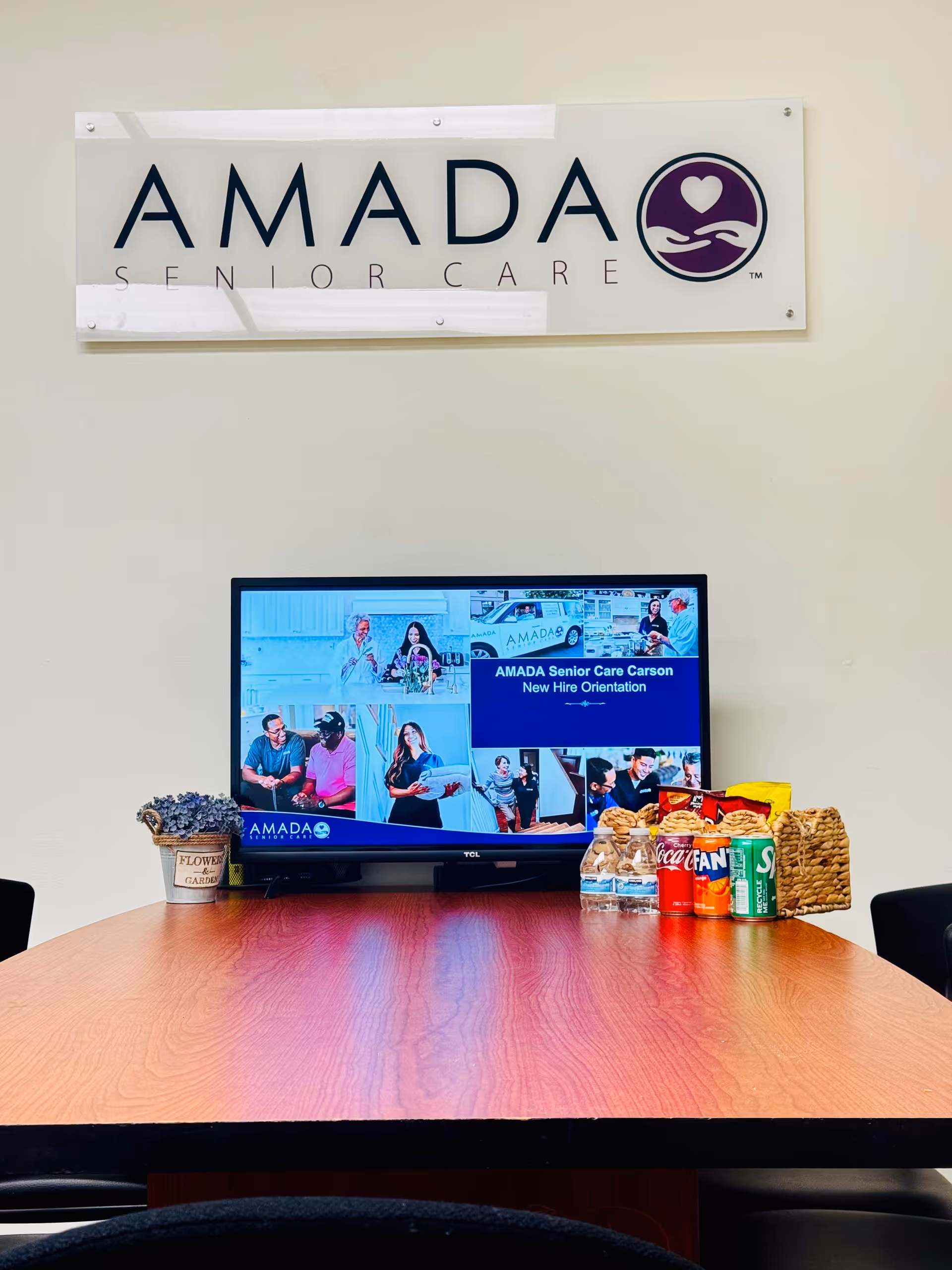 Amada Senior Care sign on wall above a TV on a wooden table.