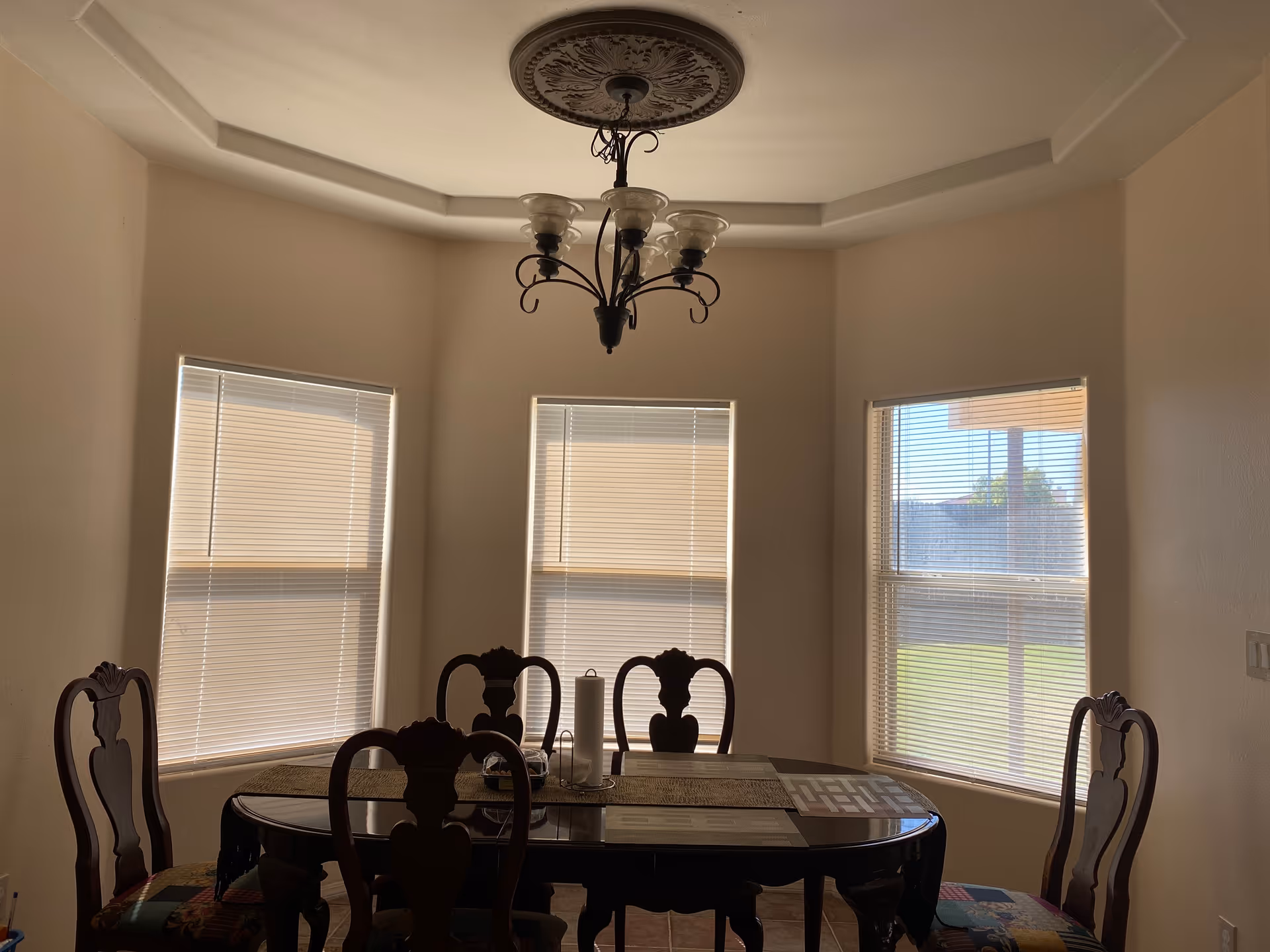 Dining room with a dark wood table, ornate chairs, chandelier, and windows.