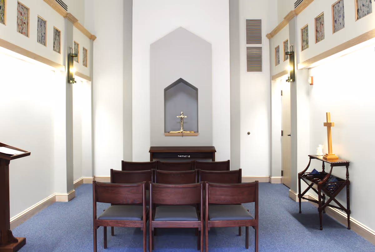 Small chapel inside a hospice facility with wooden chairs facing an altar.