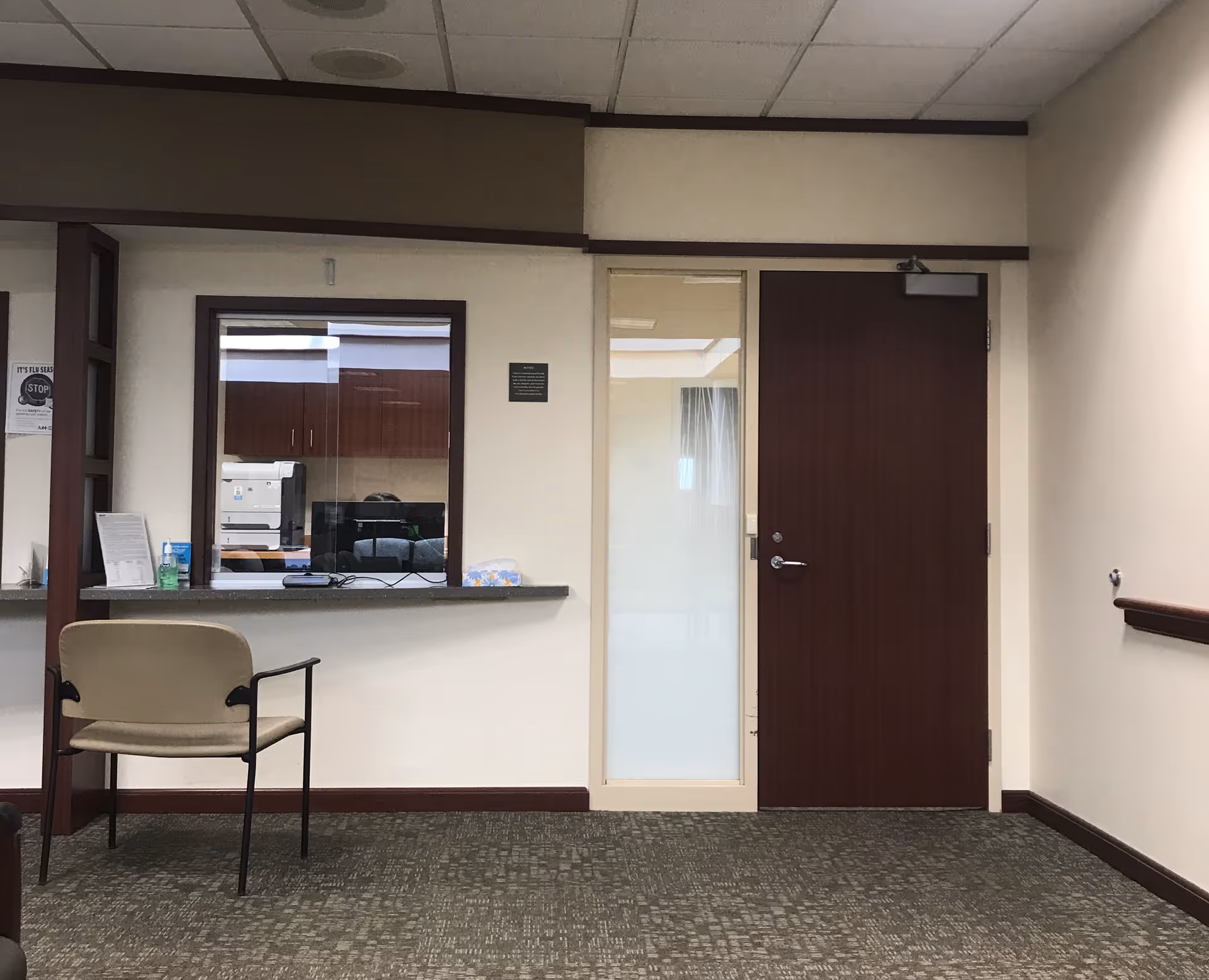 Interior reception area with a counter window, chair, and closed door.