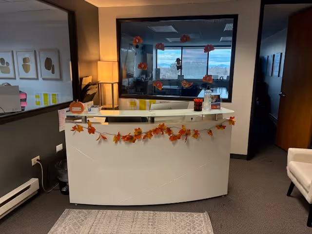 Reception desk inside a senior facility lobby, autumn leaves garland, windowed office beyond.