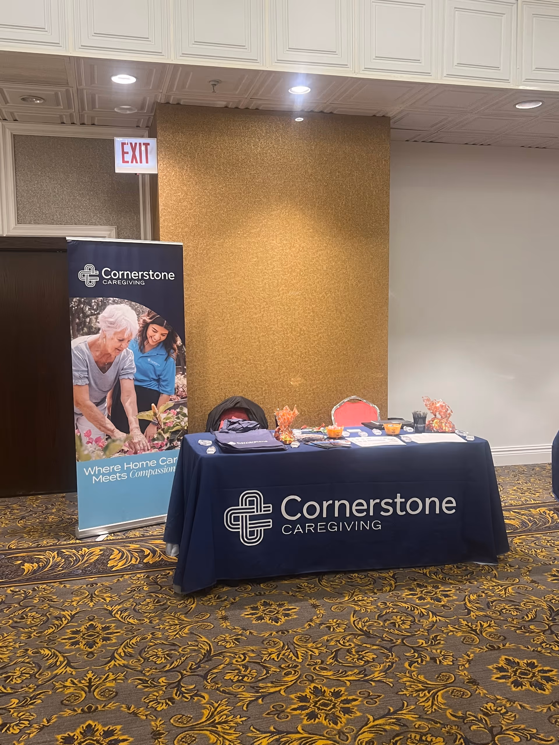 Indoor exhibition booth with Cornerstone Caregiving banner and table displaying logo.