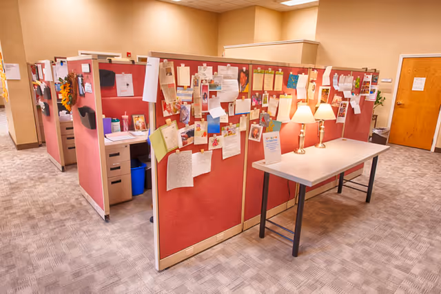Red cubicles with flyers and bulletin boards in a hallway office area.