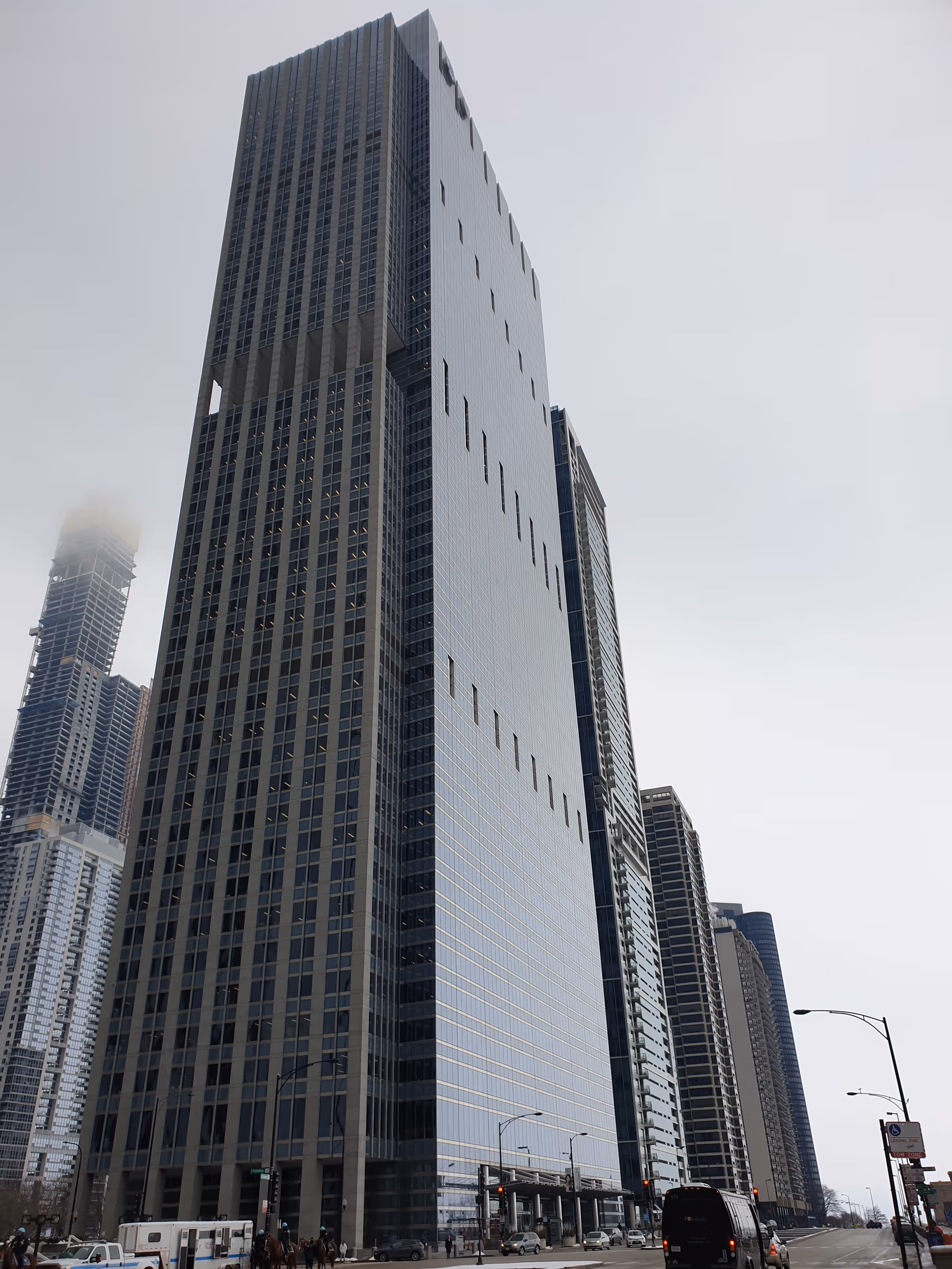A tall modern glass skyscraper dominates a city street with surrounding high-rises and traffic.