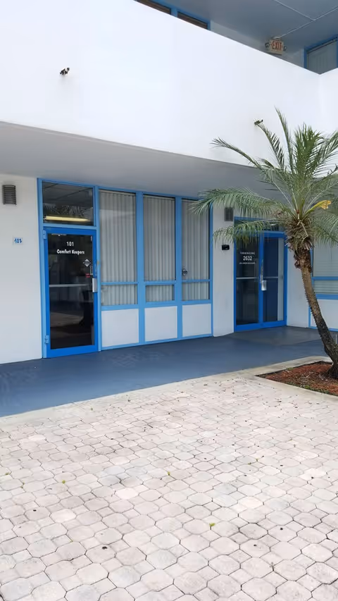 Exterior view of Comfort Keepers Home Care entrance with blue-framed doors and a palm tree.