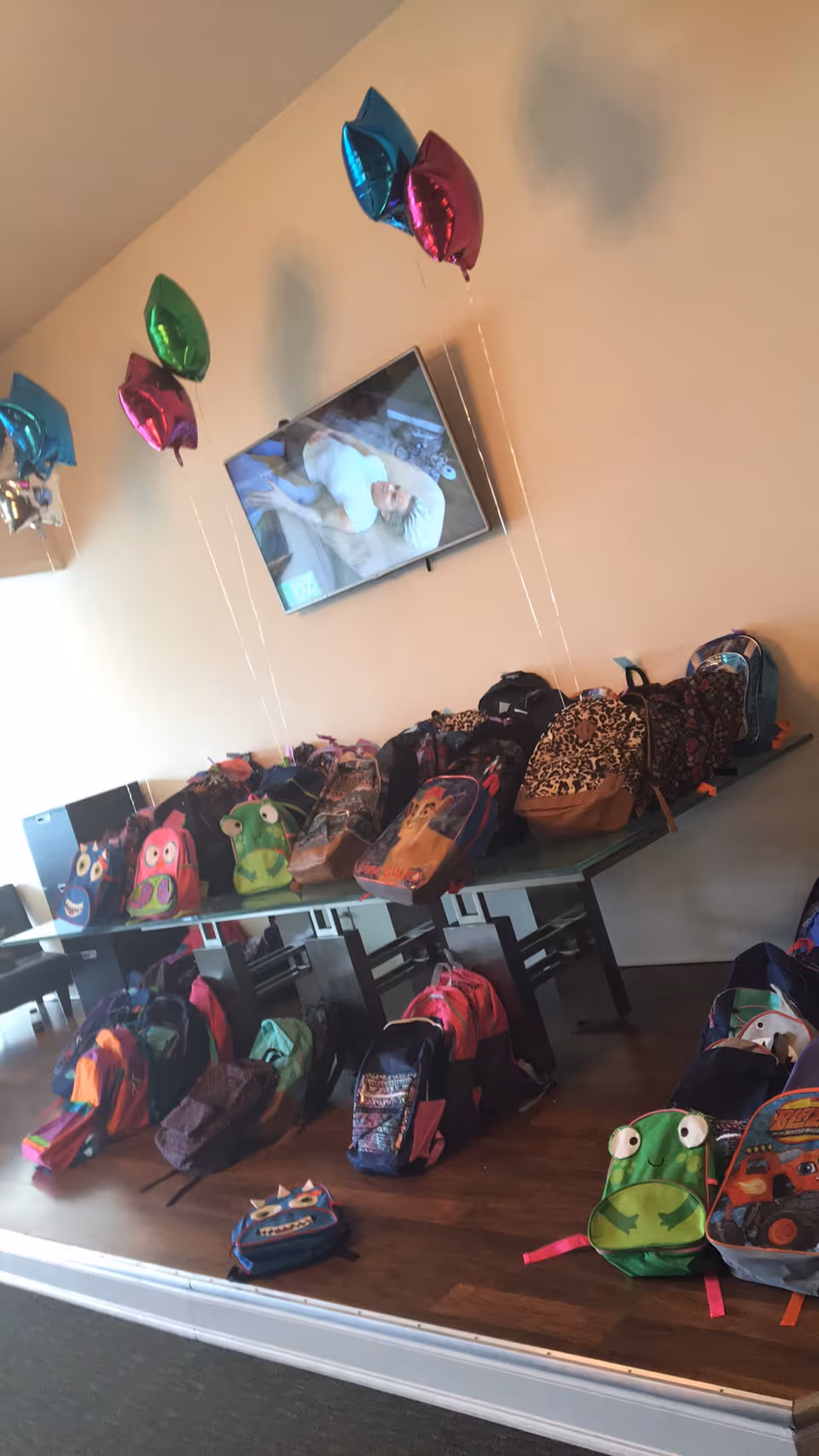 Backpacks lined on tables in a colorful indoor room with balloons.