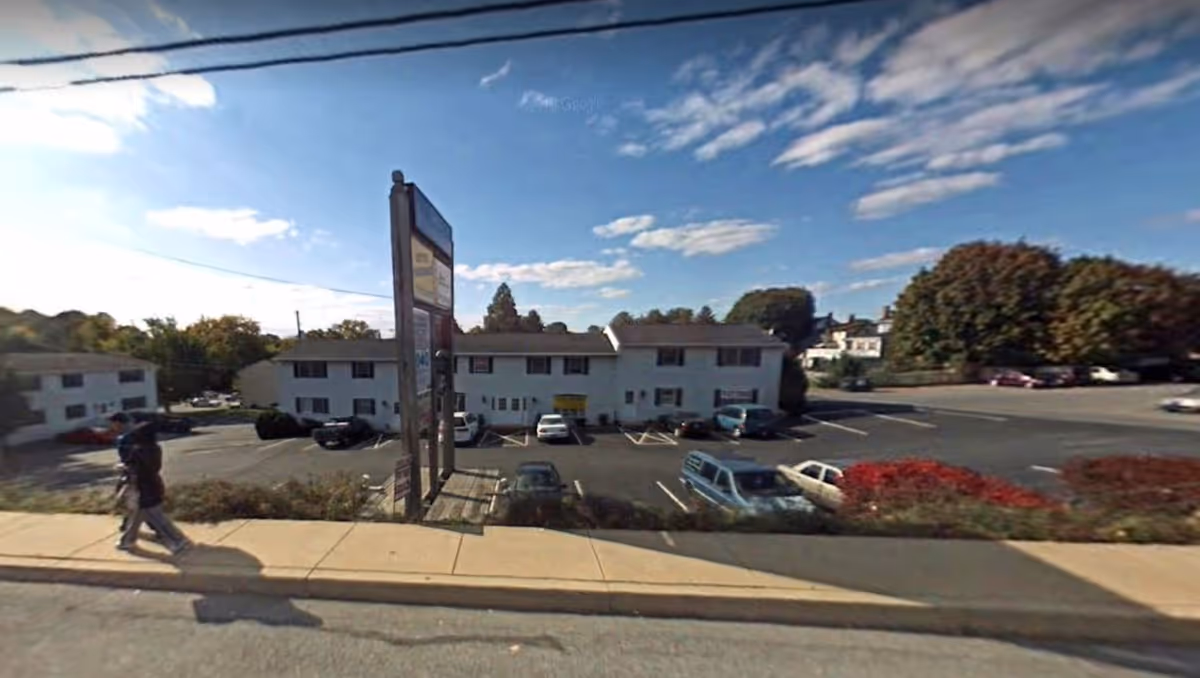 Exterior view of a two-story white senior housing building with a parking lot and sign.