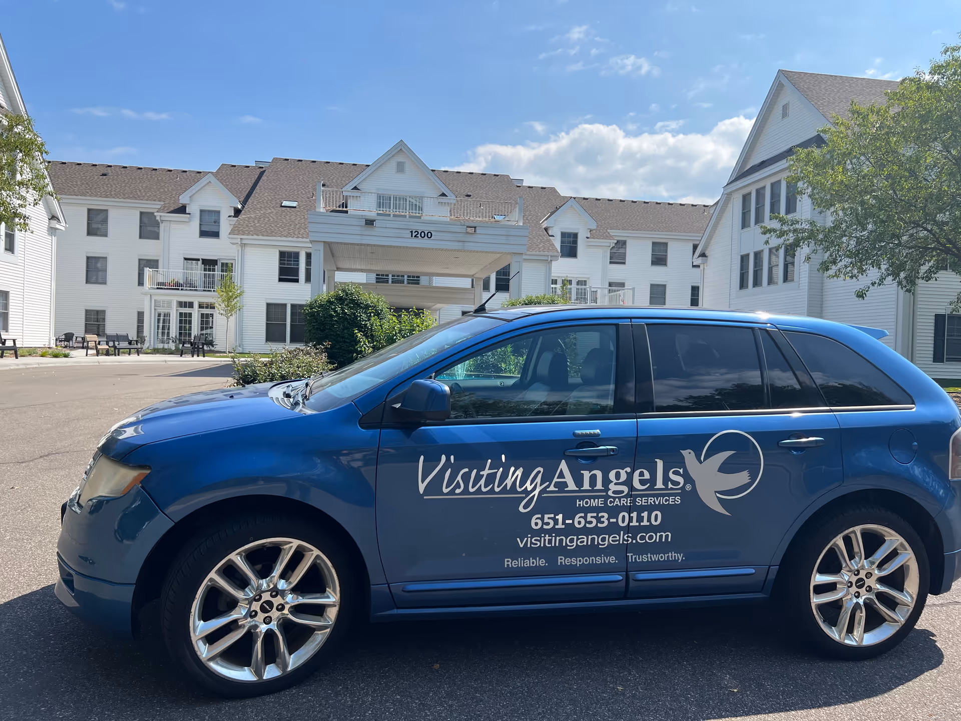Blue Visiting Angels van parked in front of a white senior living facility.
