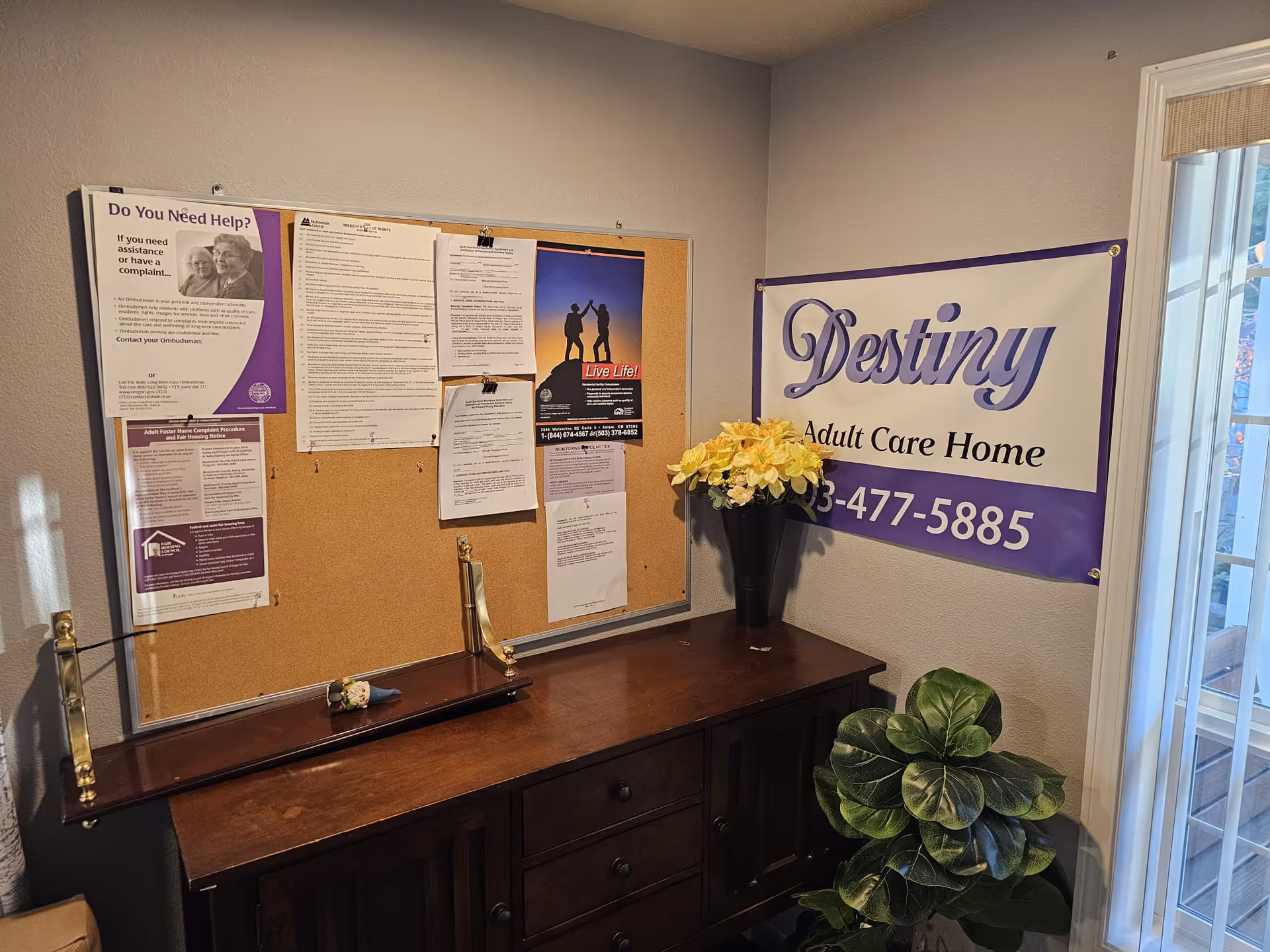Interior office area with bulletin board, Destiny Adult Care Home banner, and a potted plant.
