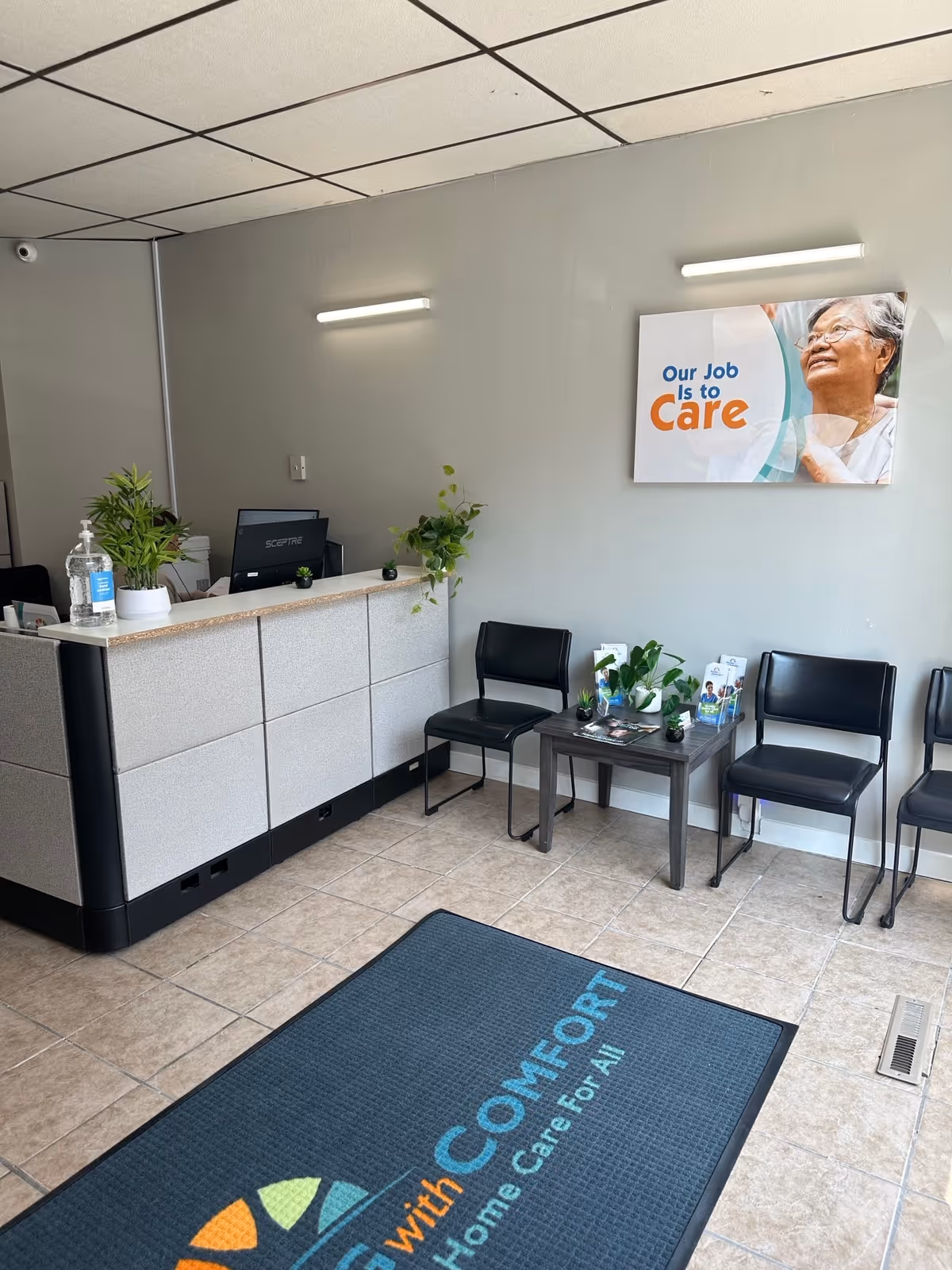 Interior lobby reception area with desk, chairs, plants, and a care poster.