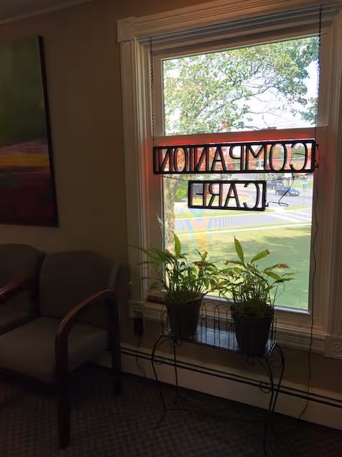 Interior living area with chairs, a window sign, and potted plants by the sill.