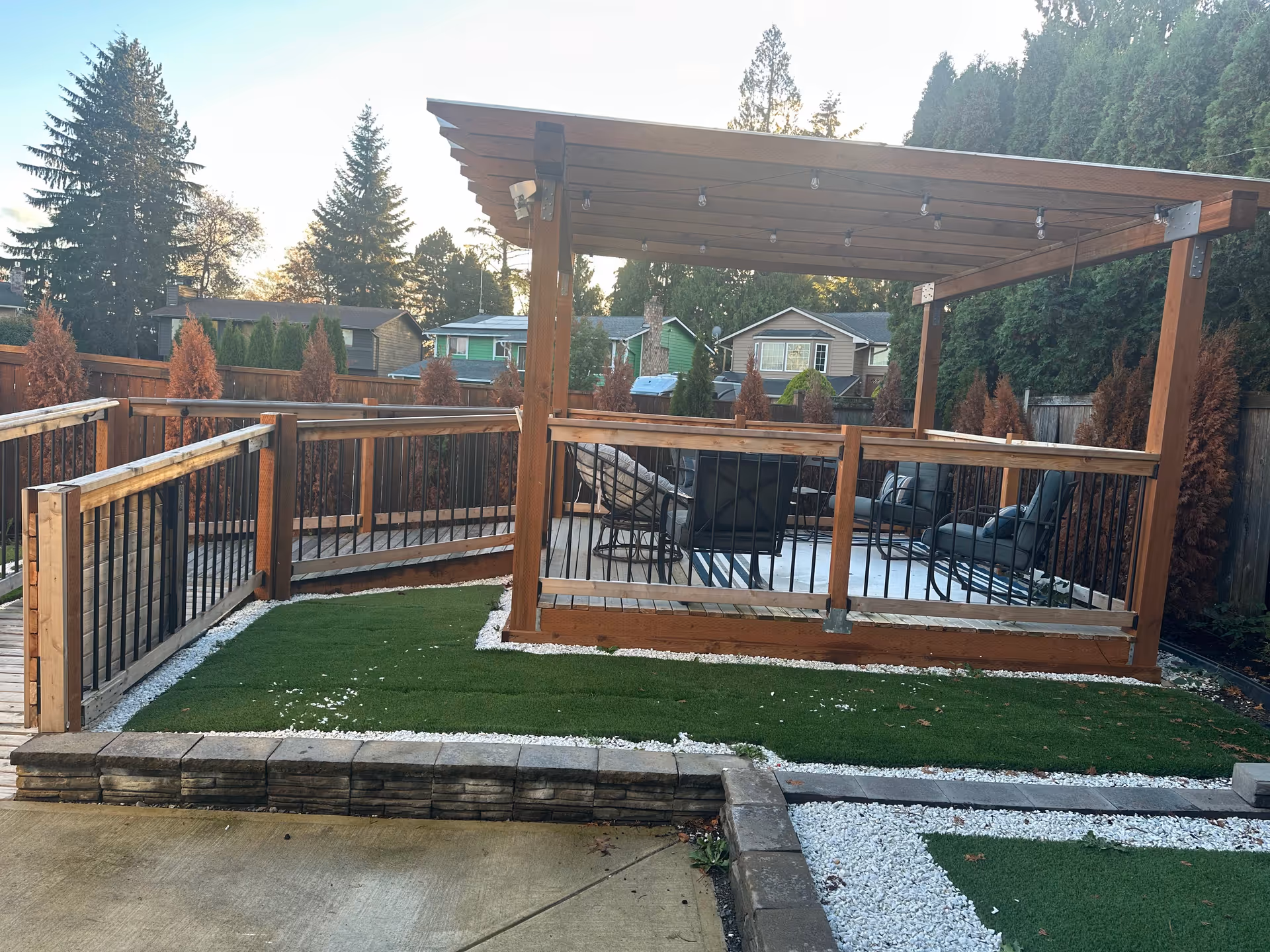 Wooden outdoor pergola with seating on a raised deck in a fenced backyard.