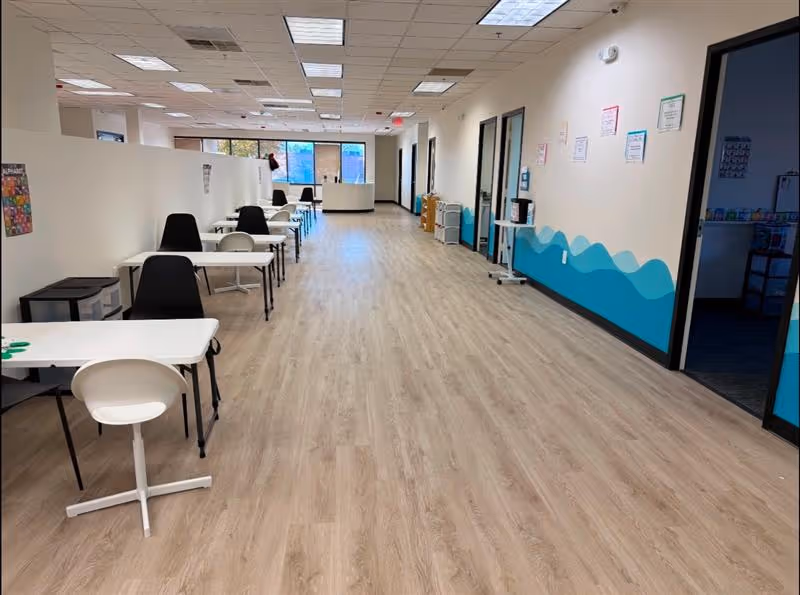 Long hallway in a facility with desks, chairs, and a turquoise wave mural along the wall.