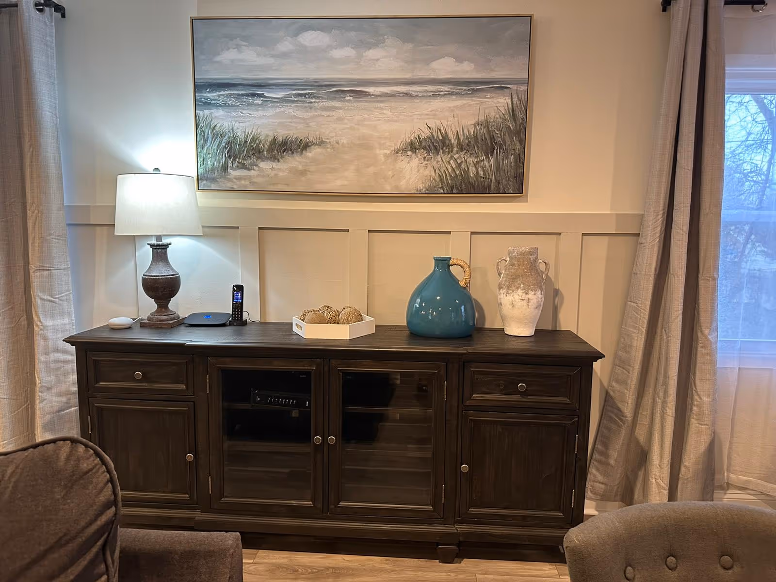 A dark wood sideboard with lamp, vases, and a beach painting in a cozy living area.