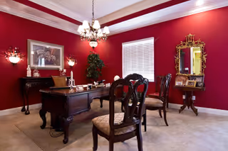 Red-walled dining room with wooden table, ornate chairs, chandelier, and sideboard.