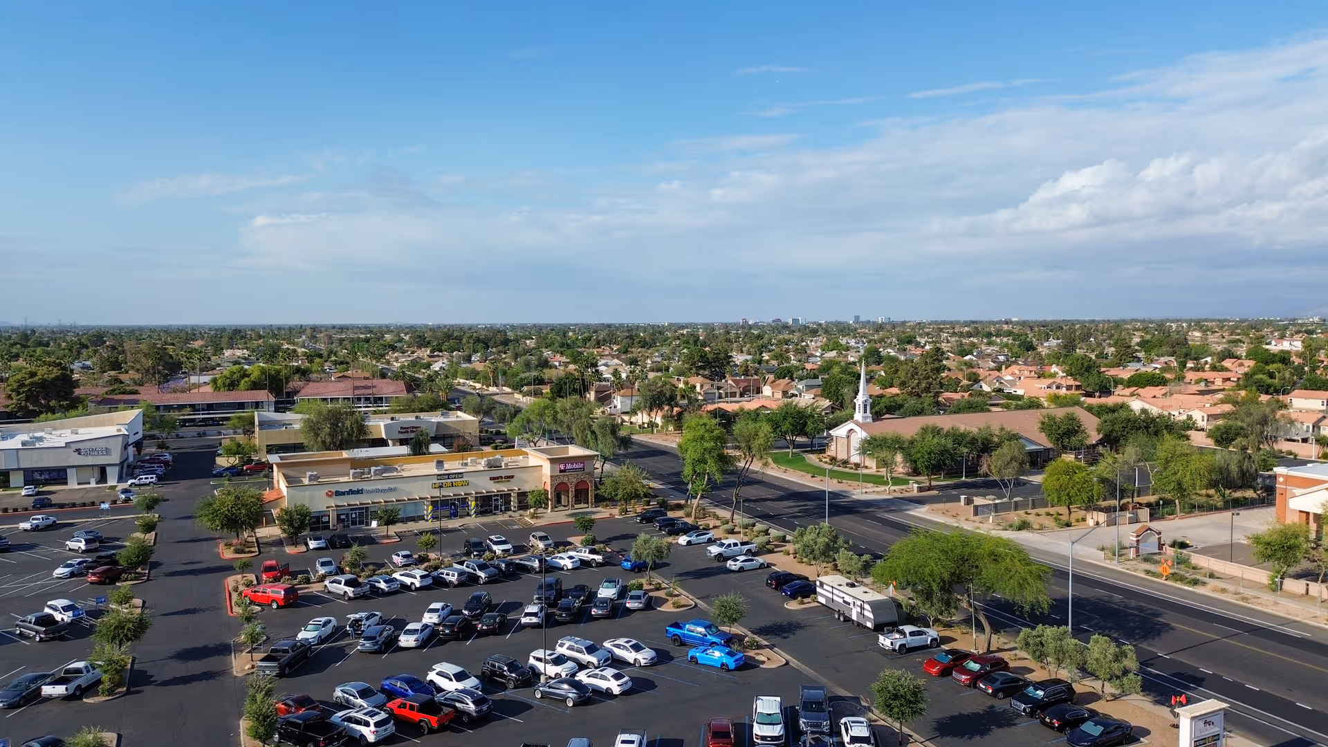 Aerial view of a shopping plaza with parking lots and surrounding streets.